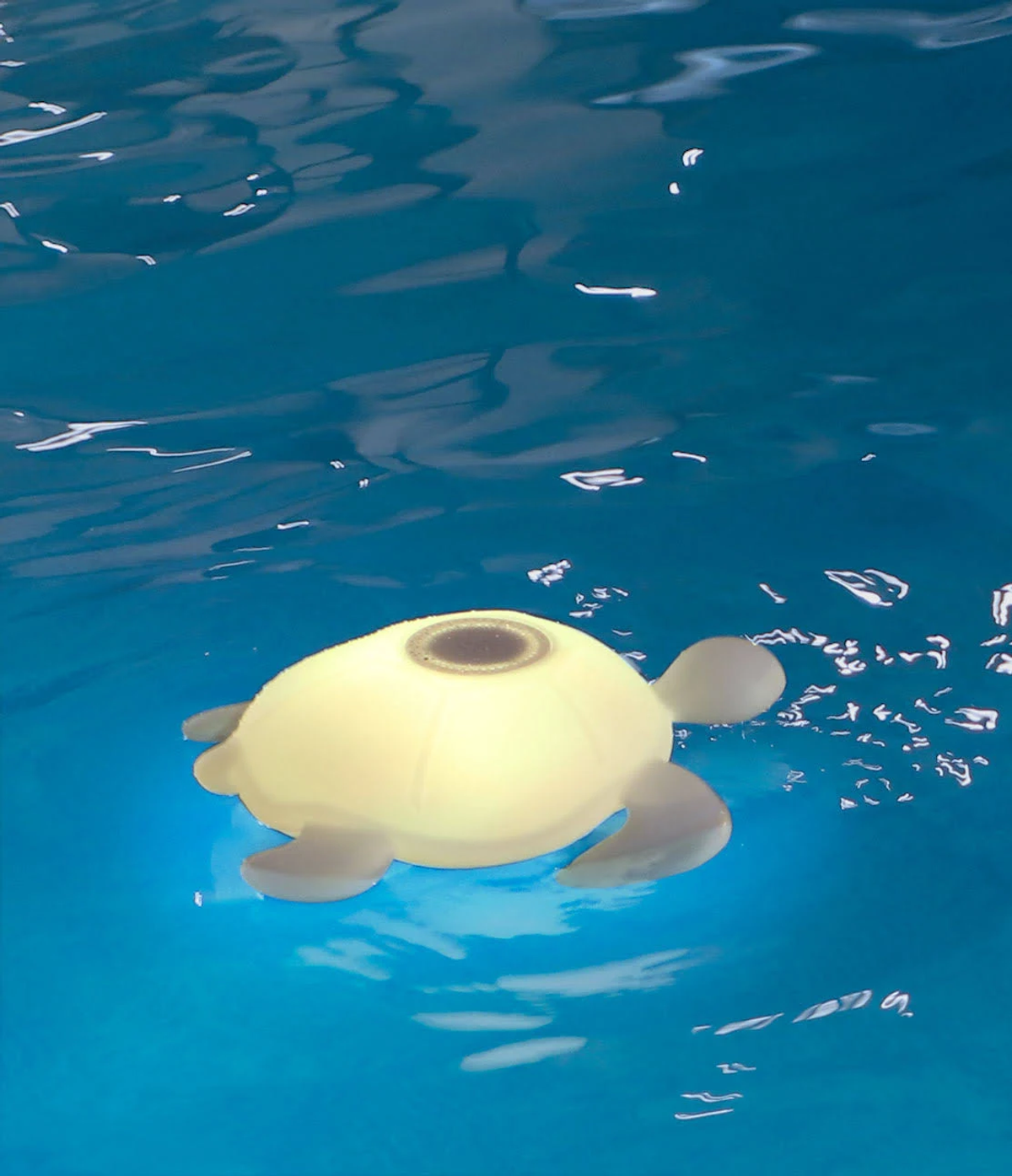 Żółte światło w kształcie żółwia unosi się w niebieskiej wodzie. Światło odbija się na wodzie.