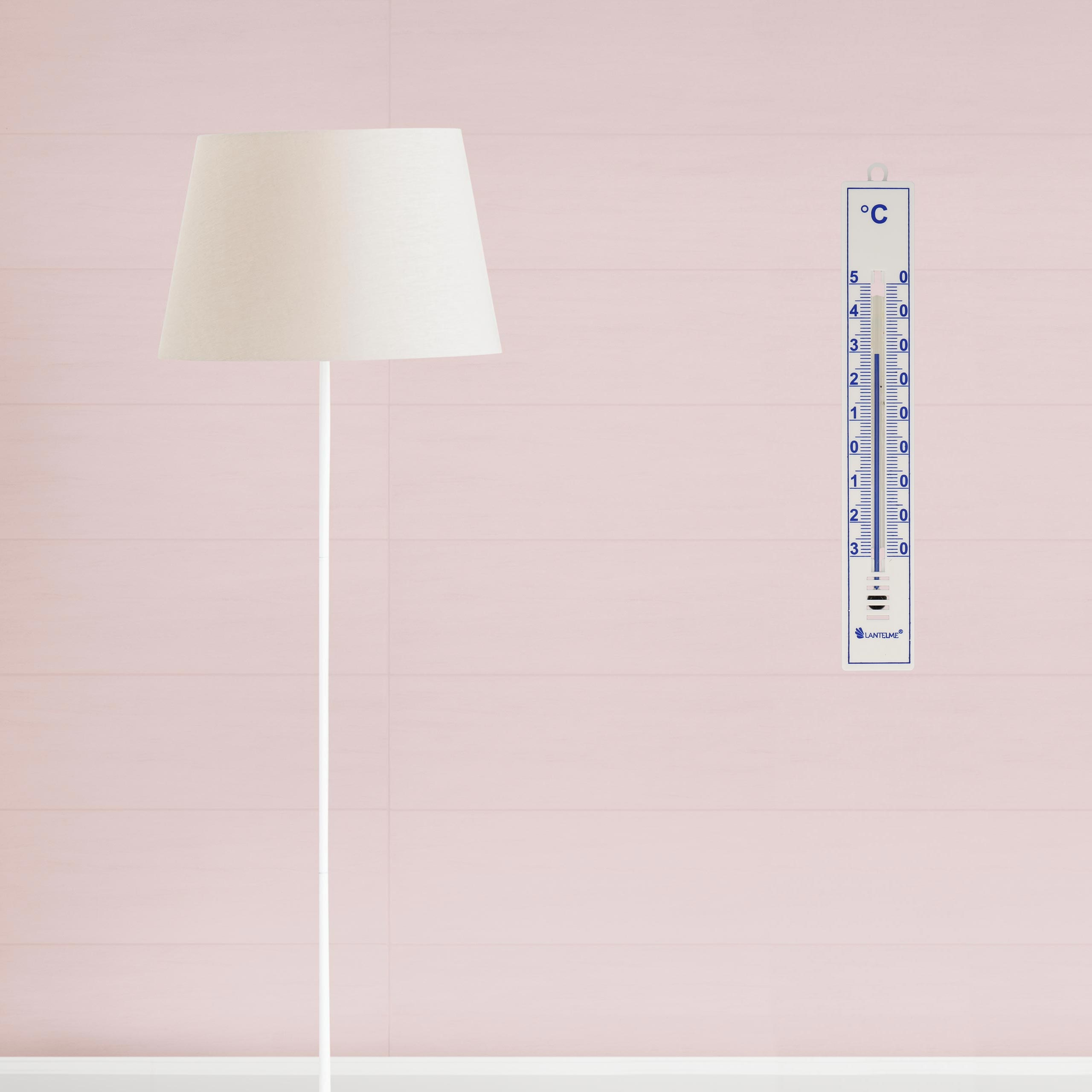 Ein Thermometer an einer rosa Wand neben einer weißen Stehlampe.