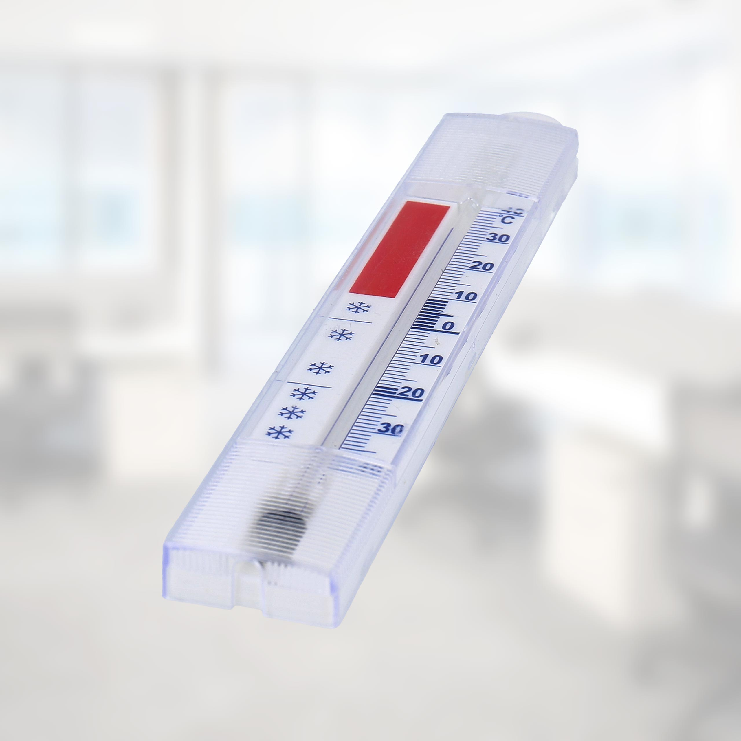 Klarer Kunststoffthermometer mit roter Skala und blauen Markierungen. Hintergrund verschwommen, Raum.