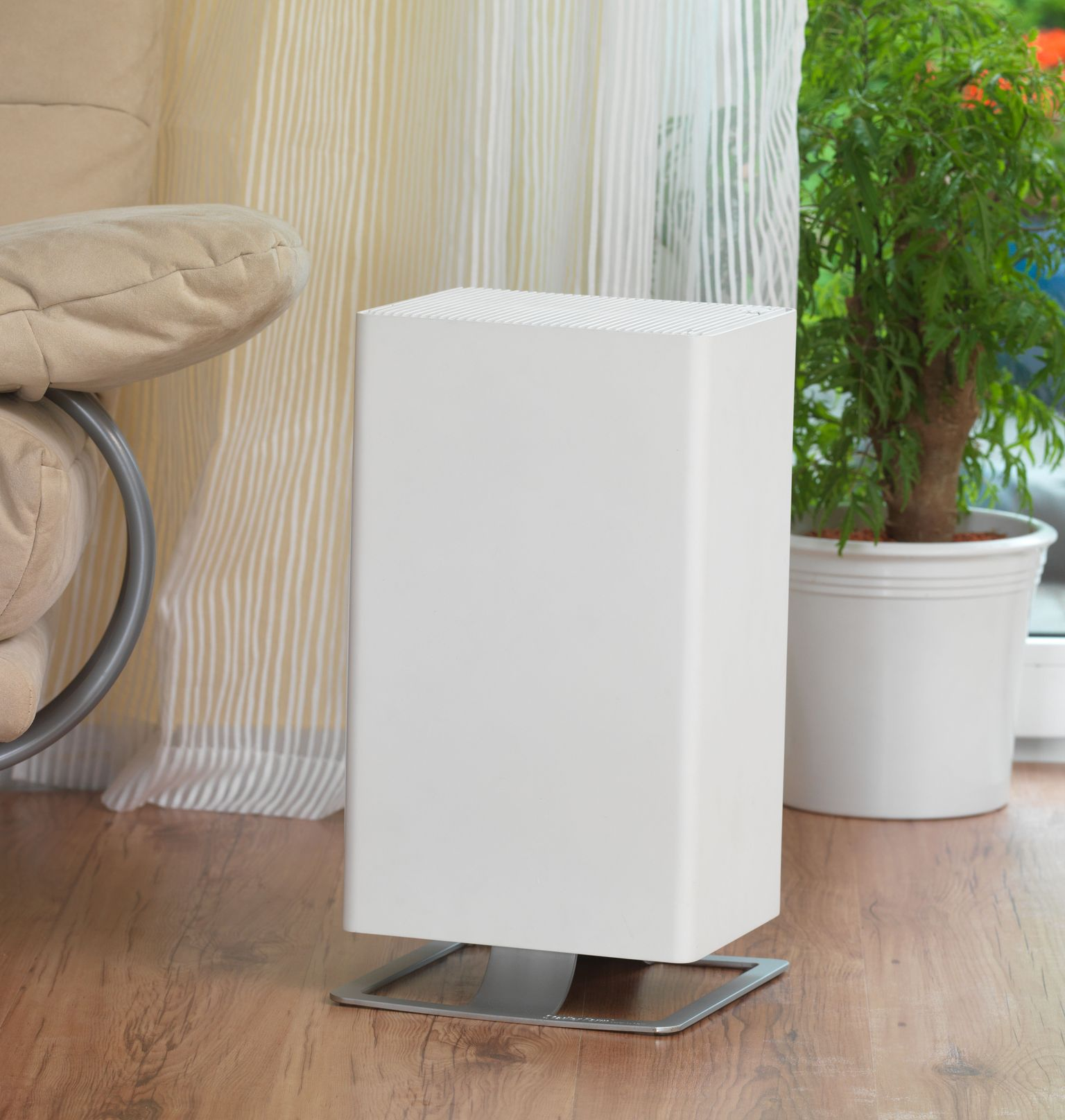 White air purifier on wood floor, near a window and a plant.