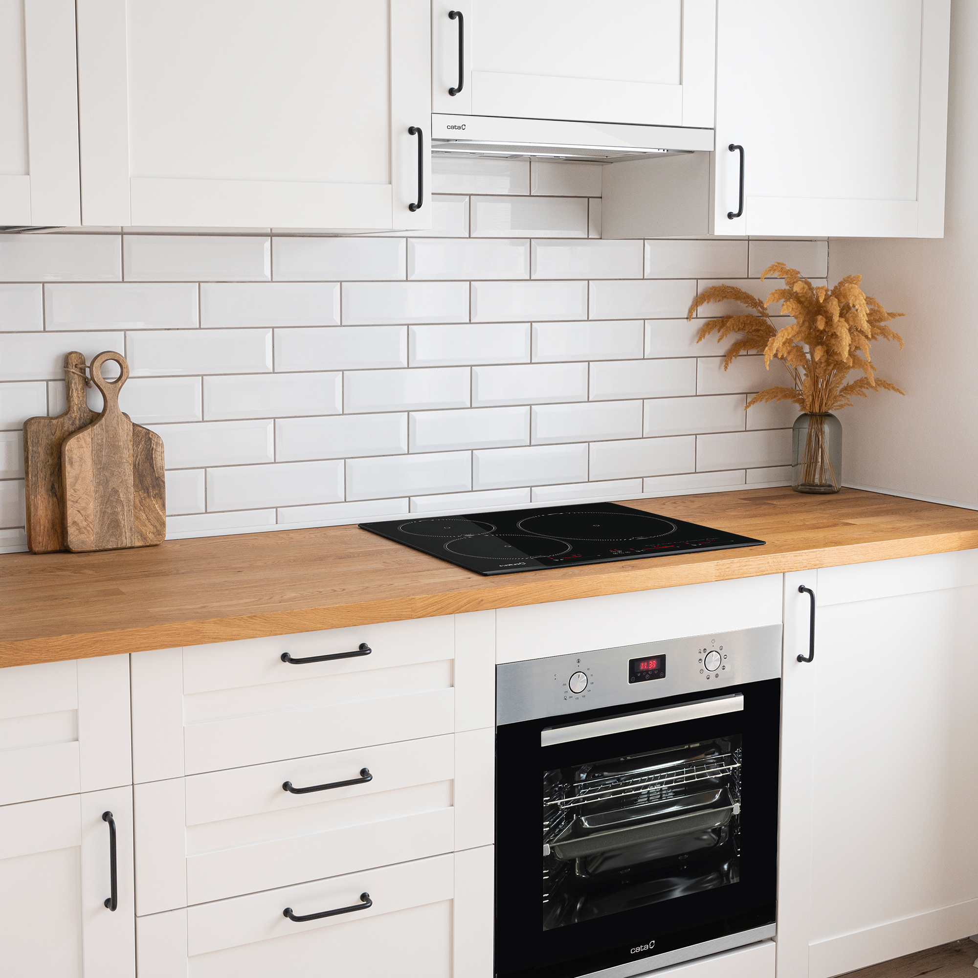 Una cocina moderna con gabinetes blancos, encimera de madera y una placa negra, con horno abajo.