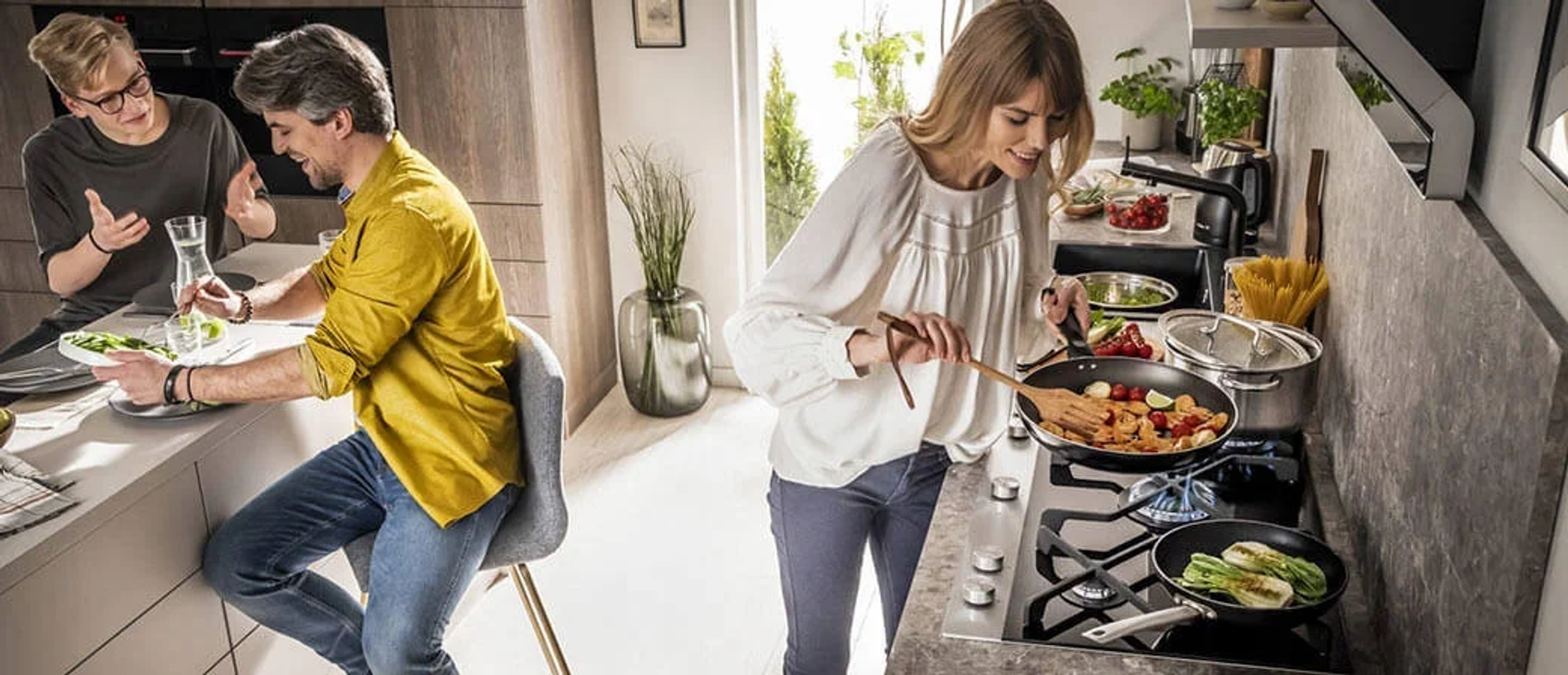 Persone che cucinano in una cucina moderna. Una donna cucina, due uomini mangiano.