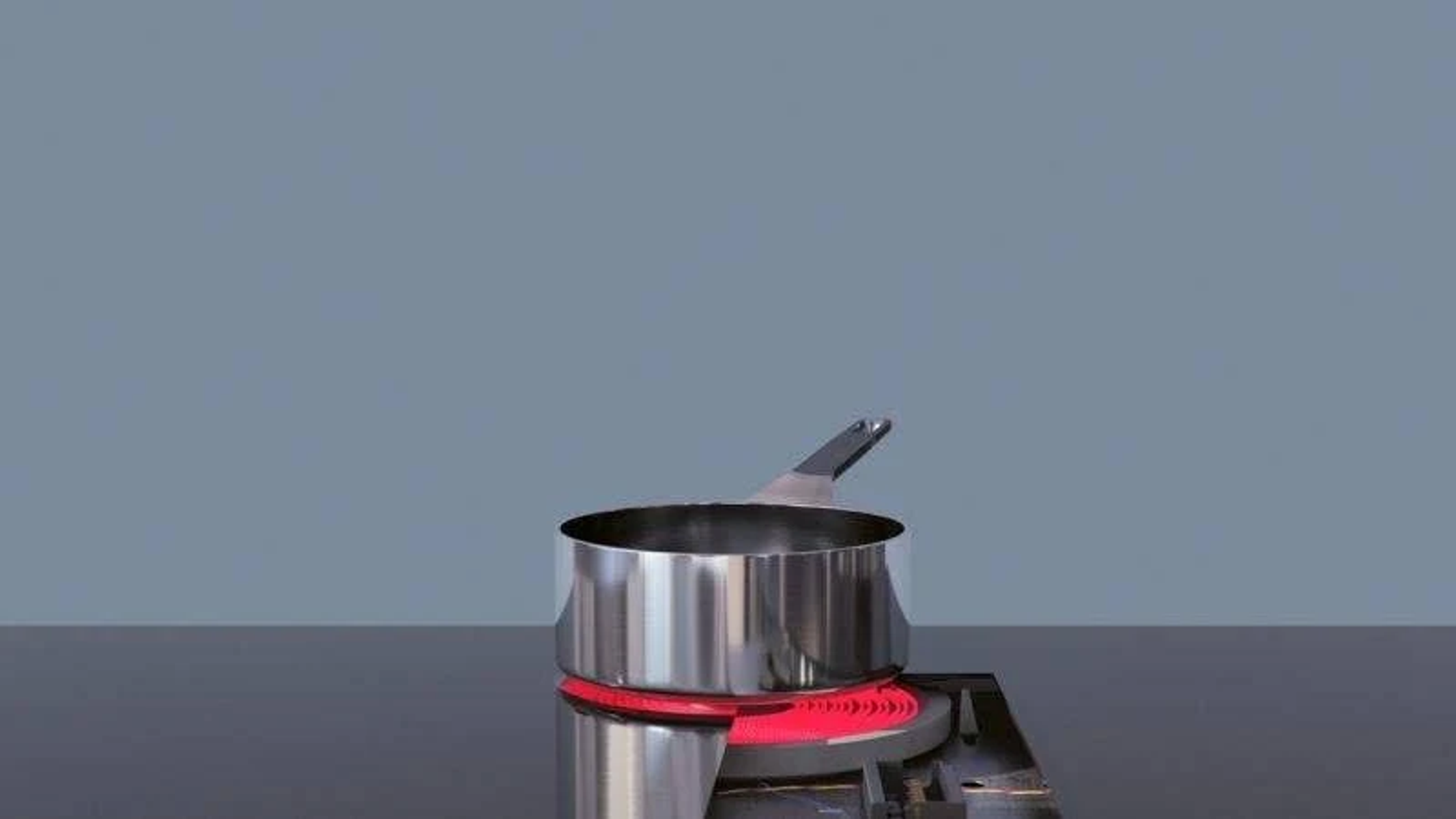 Garnek ze stali nierdzewnej na czerwonym palniku na tle niebiesko-szarej ściany.