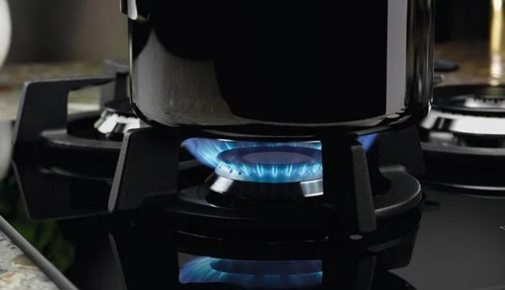 Czarny garnek na kuchence gazowej z niebieskimi płomieniami. Zbliżenie na palnik i garnek.
