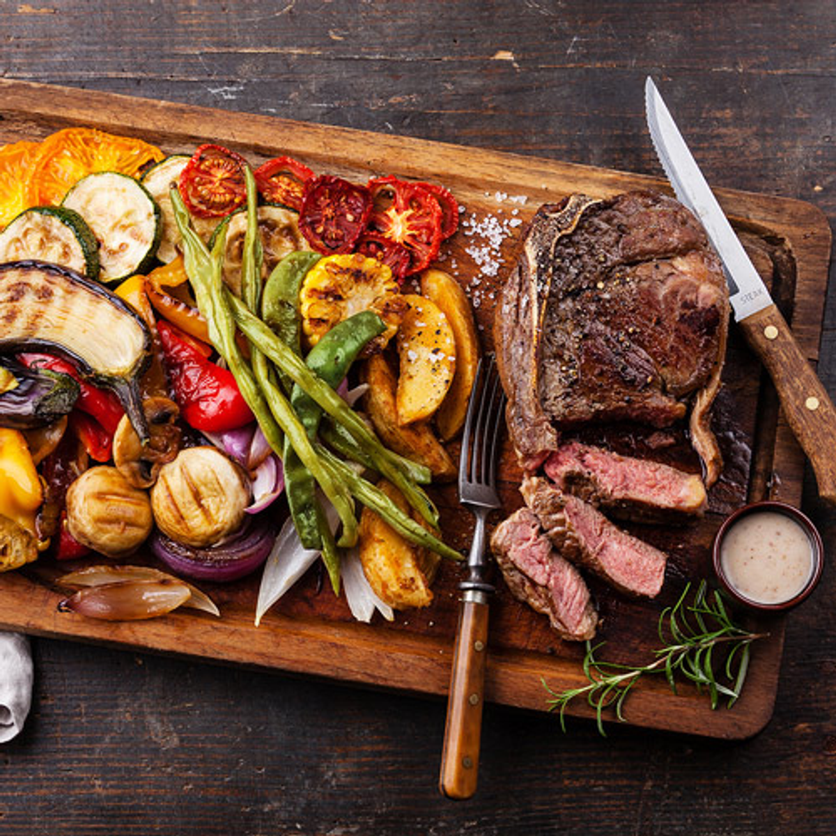 Gegrilltes Steak mit Gemüse auf einem hölzernen Schneidebrett.