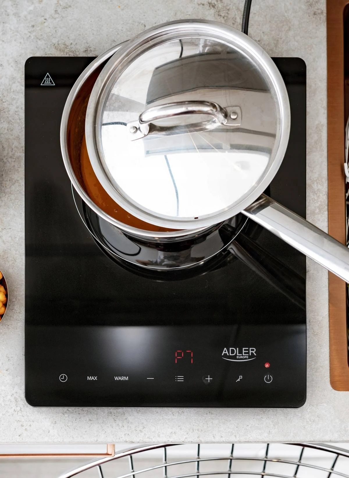 Czarna płyta indukcyjna z garnkiem i pokrywką. Wyświetlacz cyfrowy pokazuje '87'. Widok z góry.