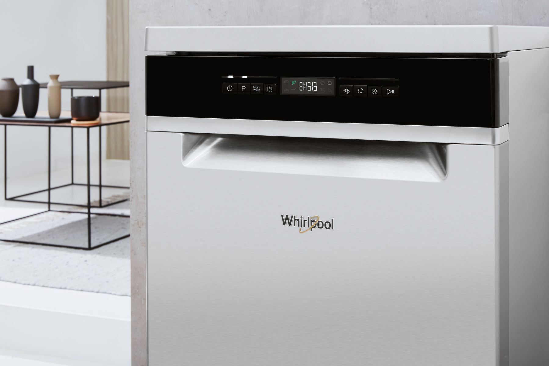 Primo piano di una lavastoviglie argentata con pannello di controllo, logo Whirlpool e sfondo sfocato.
