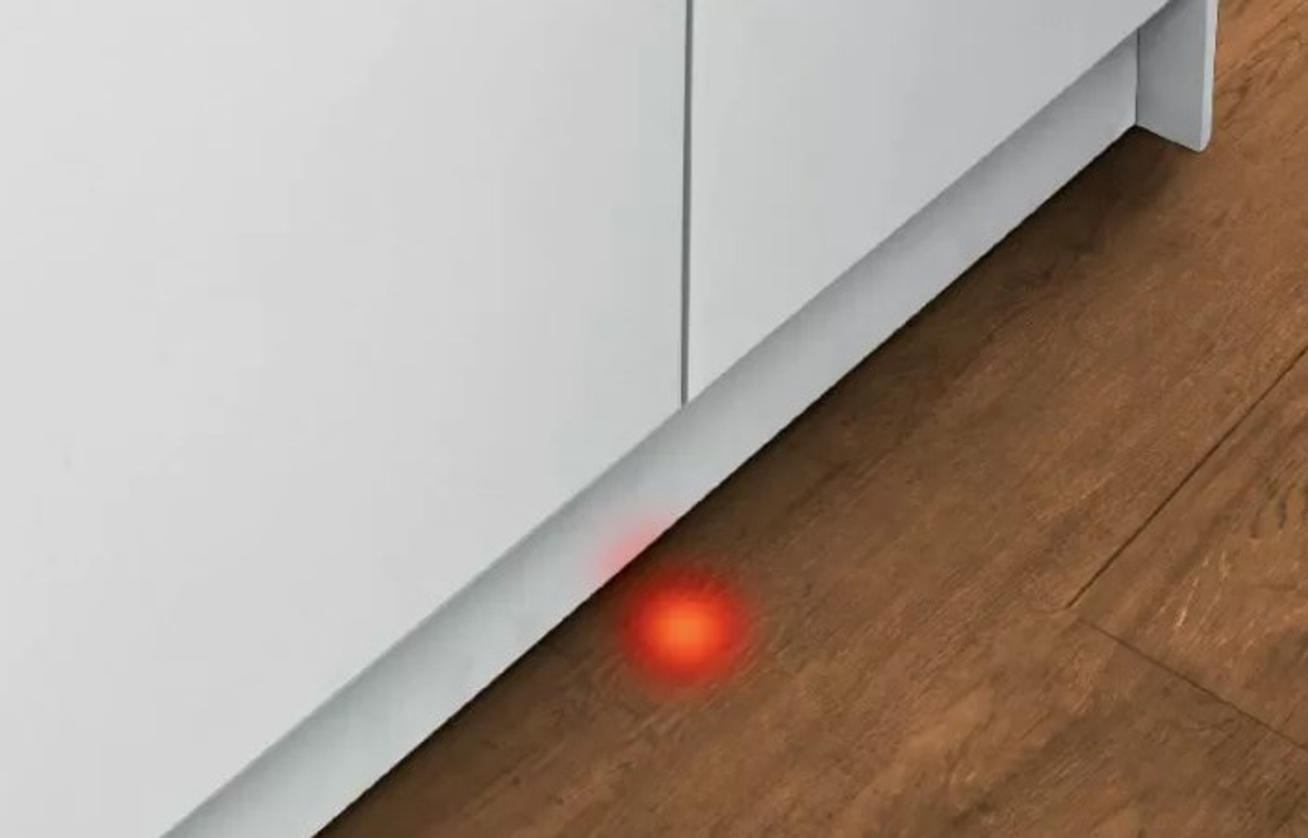 Luce rossa su pavimento in legno, vicino a elettrodomestico bianco, indica funzione.