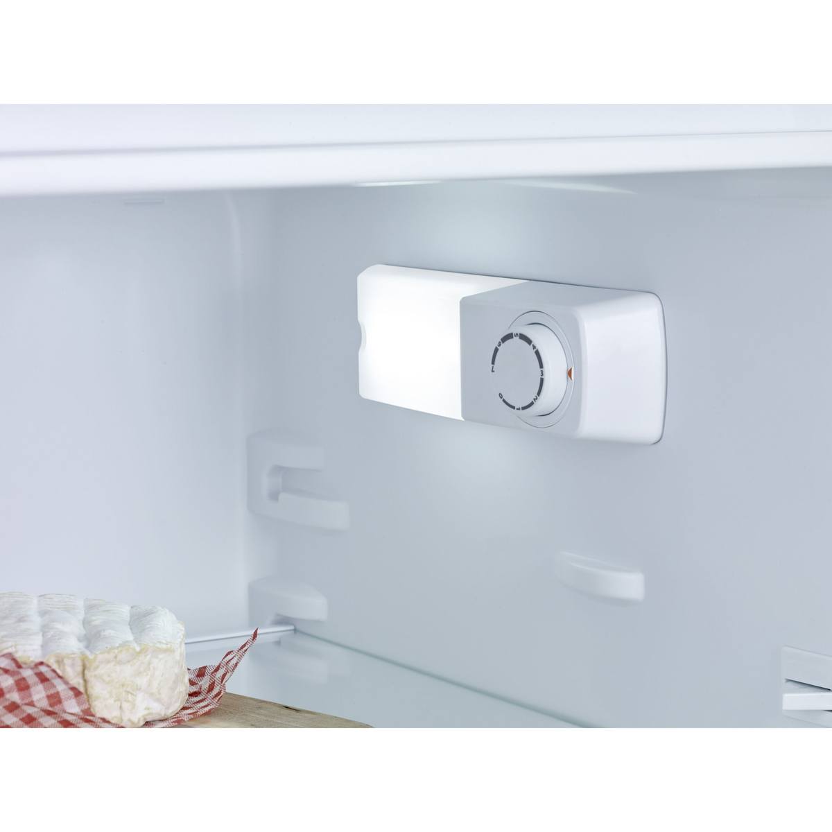 Im Kühlschrank: Käse auf einem Holzbrett, ein Licht und ein Drehregler.