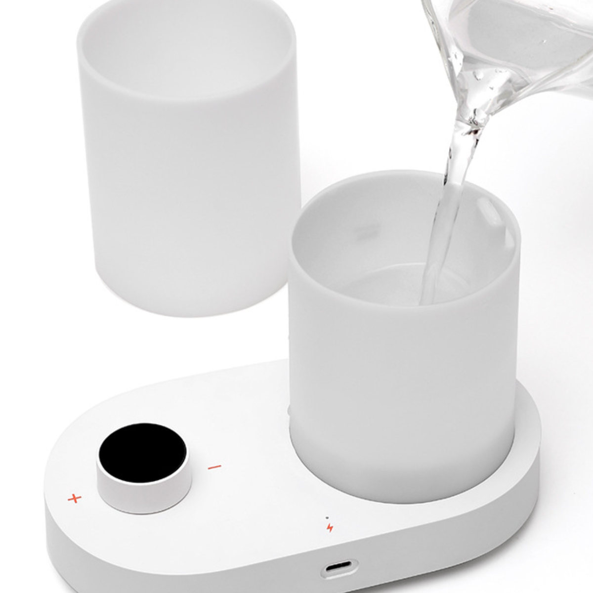 Wasser gießt in einen weißen Becher auf einem weißen Tablett mit einem Drehregler und einem anderen leeren Becher.
