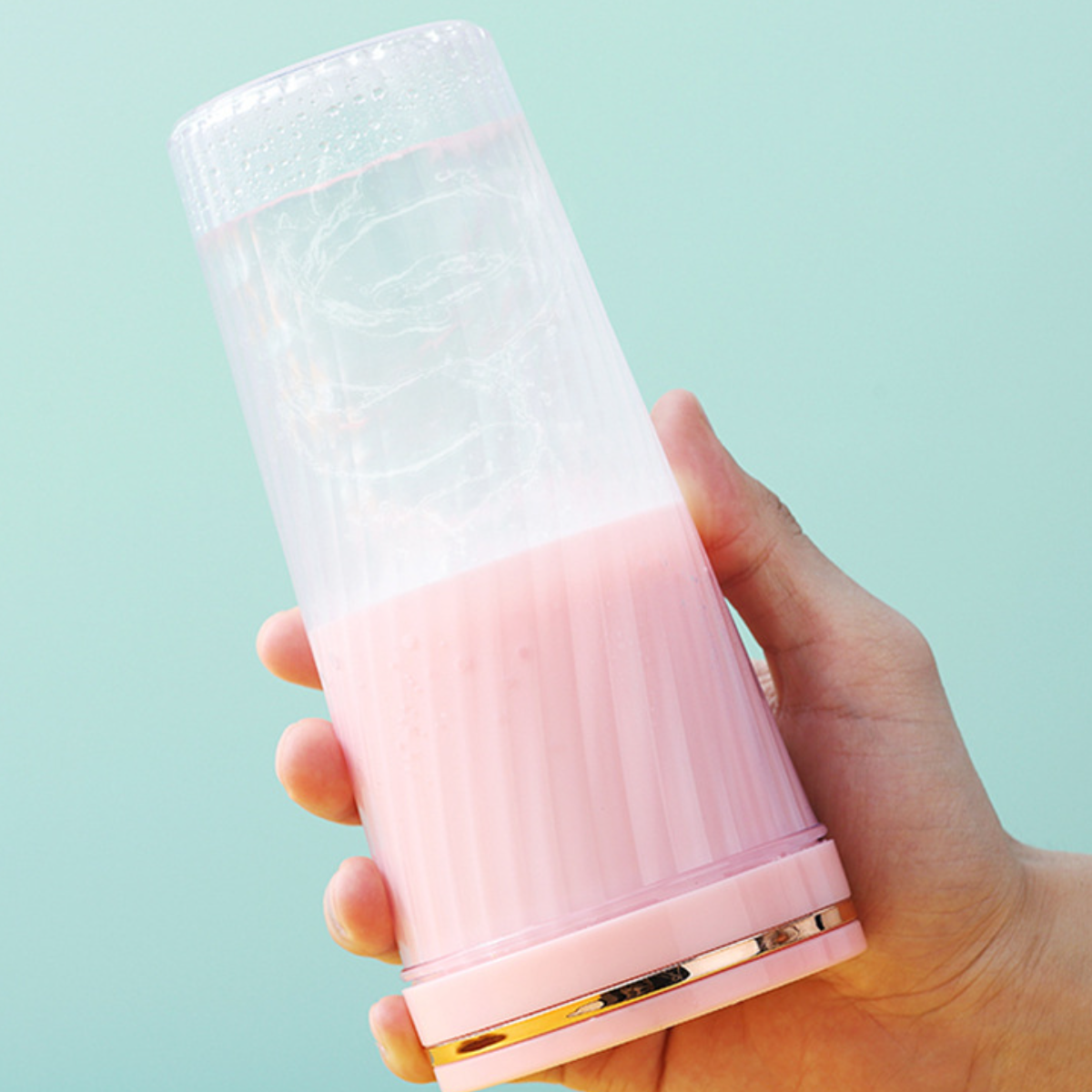 Hand hält einen pinkfarbenen, geriffelten, tragbaren Mixer, gefüllt mit rosa Flüssigkeit.