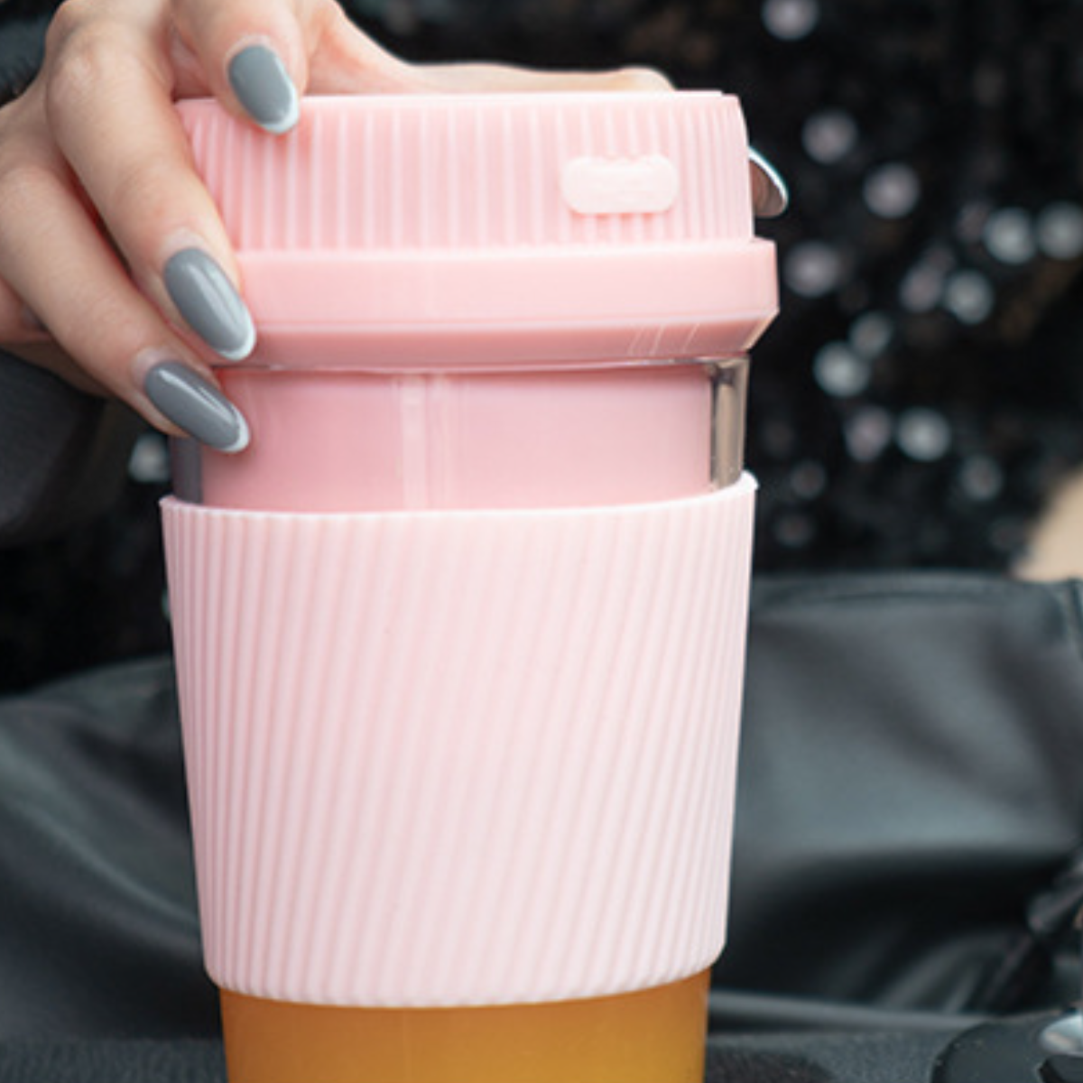 Eine Frau hält einen rosa-weißen Reisebecher. Der Becher hat einen rosa Deckel und befindet sich vor einem schwarzen Hintergrund.