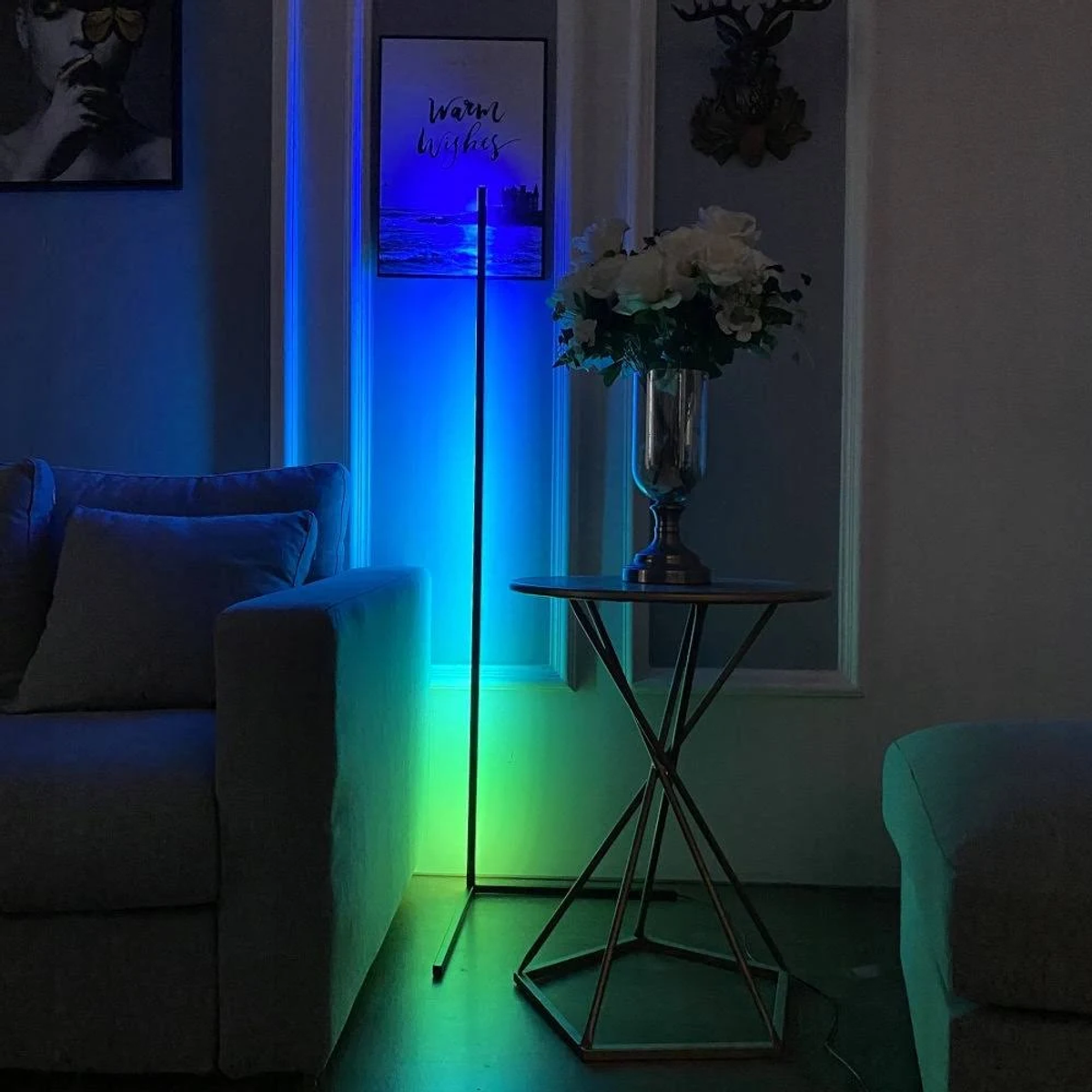 Una stanza moderna con una lampada da terra che emette luce blu e verde, accanto a un tavolo con fiori.
