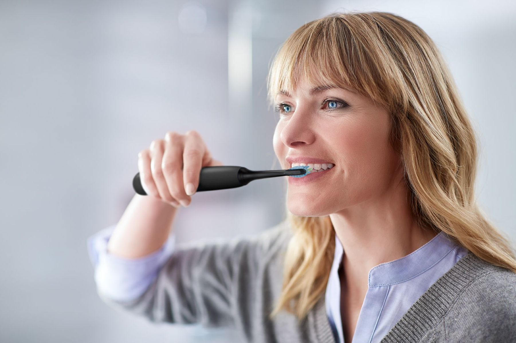 Donna che si lava i denti con uno spazzolino elettrico nero. Sorride.