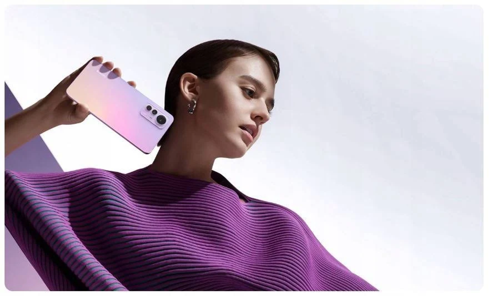 Kobieta trzymająca różowy telefon z aparatem, ubrana w fioletowy sweter.