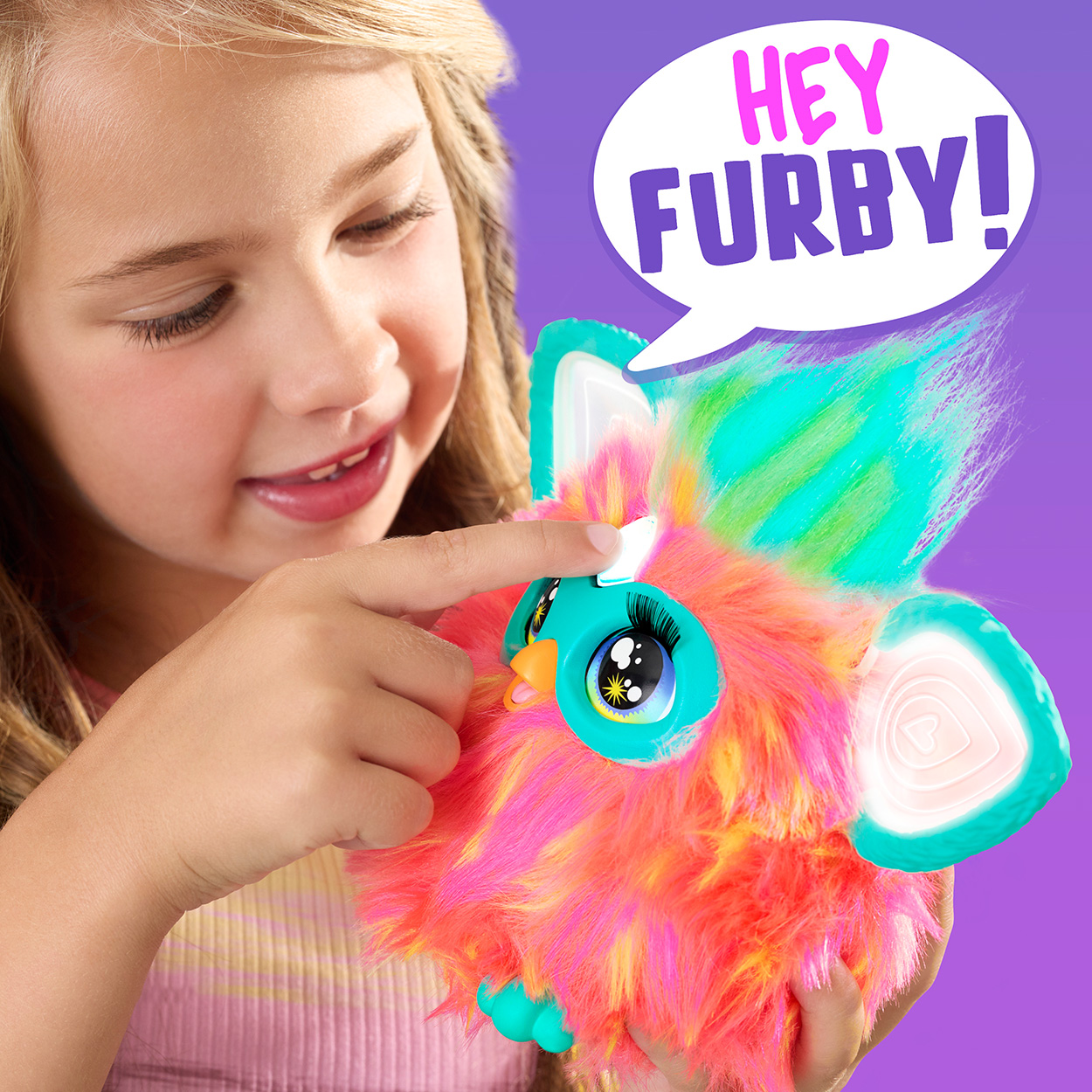 Ein Mädchen interagiert mit einem bunten Furby-Spielzeug. Eine Sprechblase sagt 'Hey Furby!'