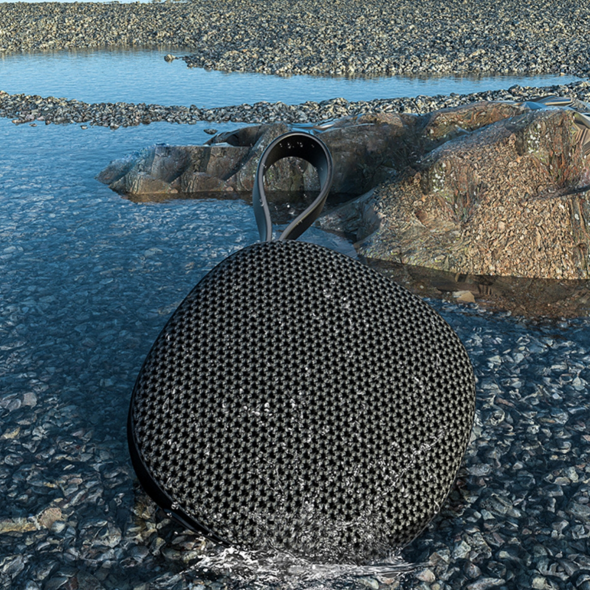 Ein schwarzer Lautsprecher sitzt im Wasser zwischen kleinen Felsen, klarem Wasser und größeren Felsen.