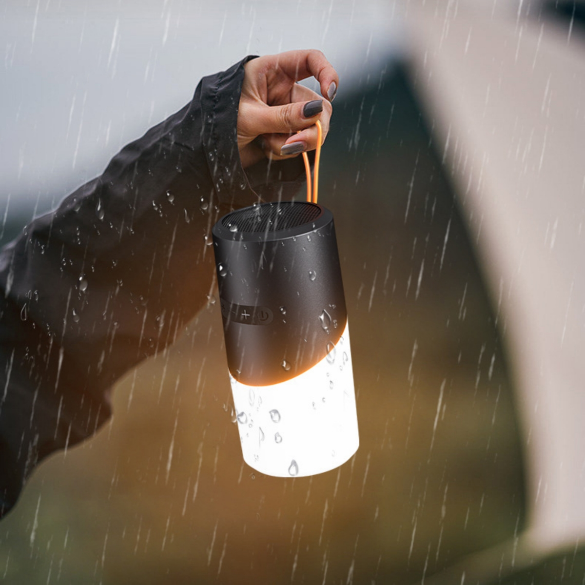 Eine schwarz-weiße zylinderförmige Laterne wird bei Regen in einer Hand gehalten. Der Boden ist beleuchtet.