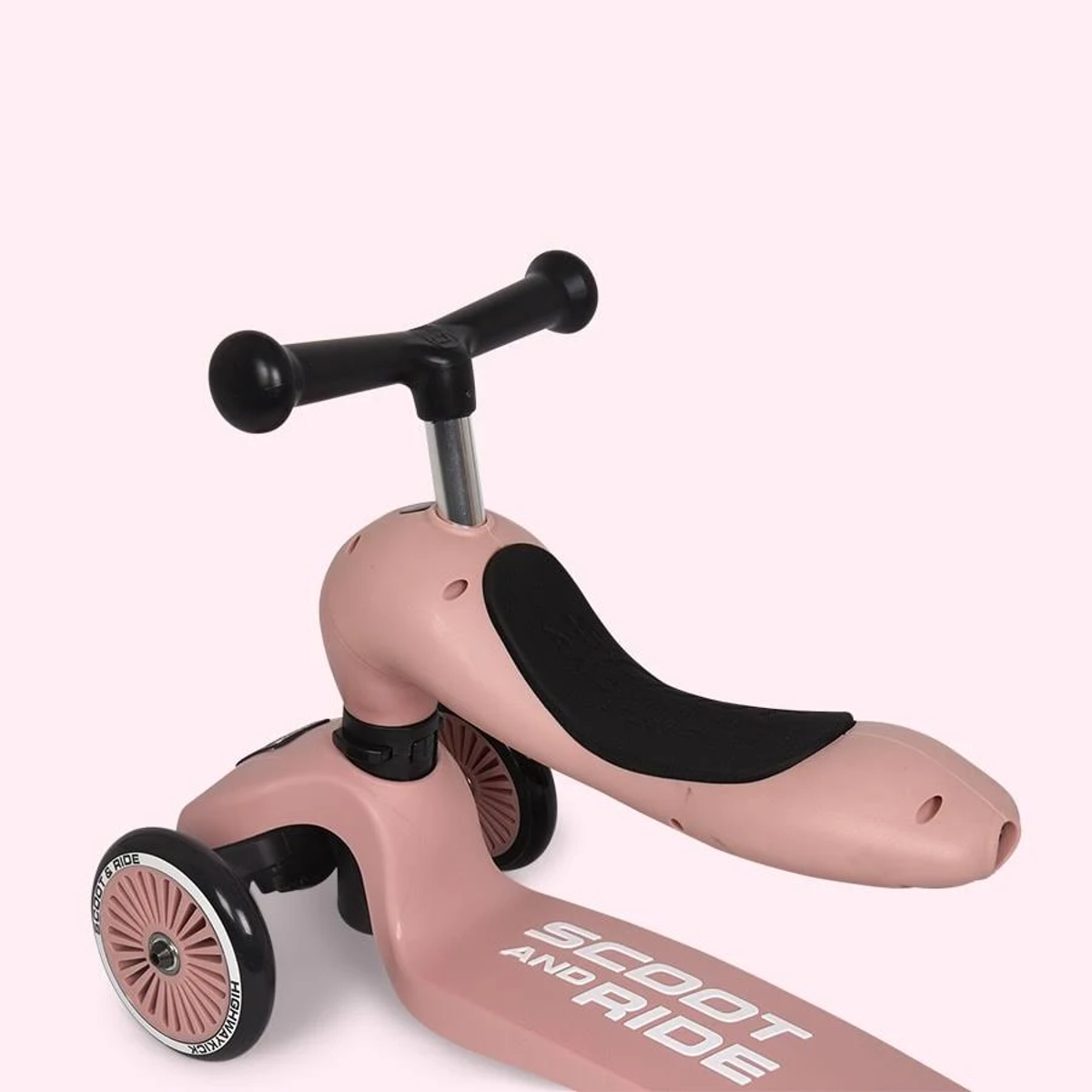 Un trotteur rose avec guidon et siège noirs sur fond rose.