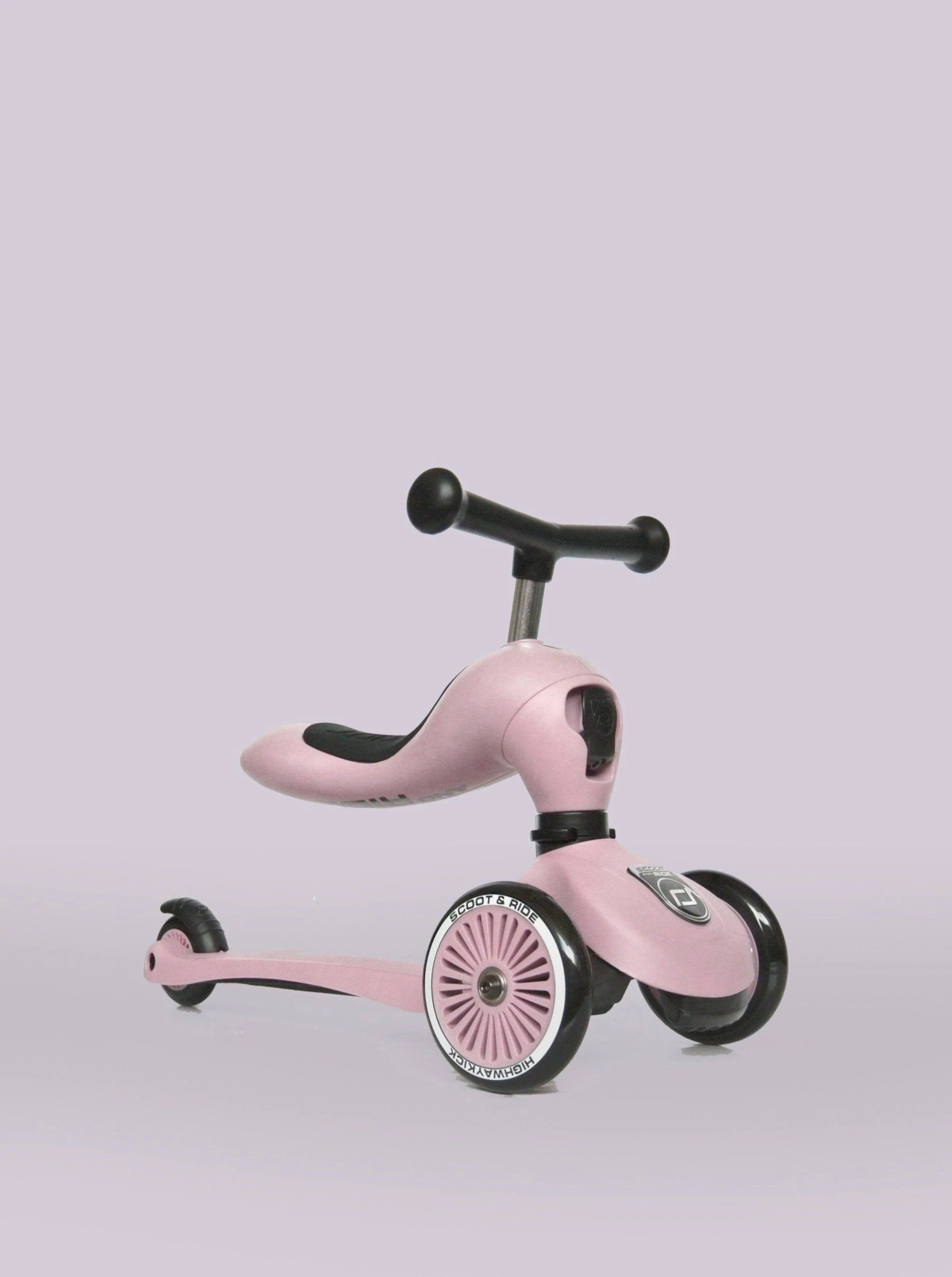 Un trotteur rose à trois roues avec guidon et siège noirs sur fond lilas.