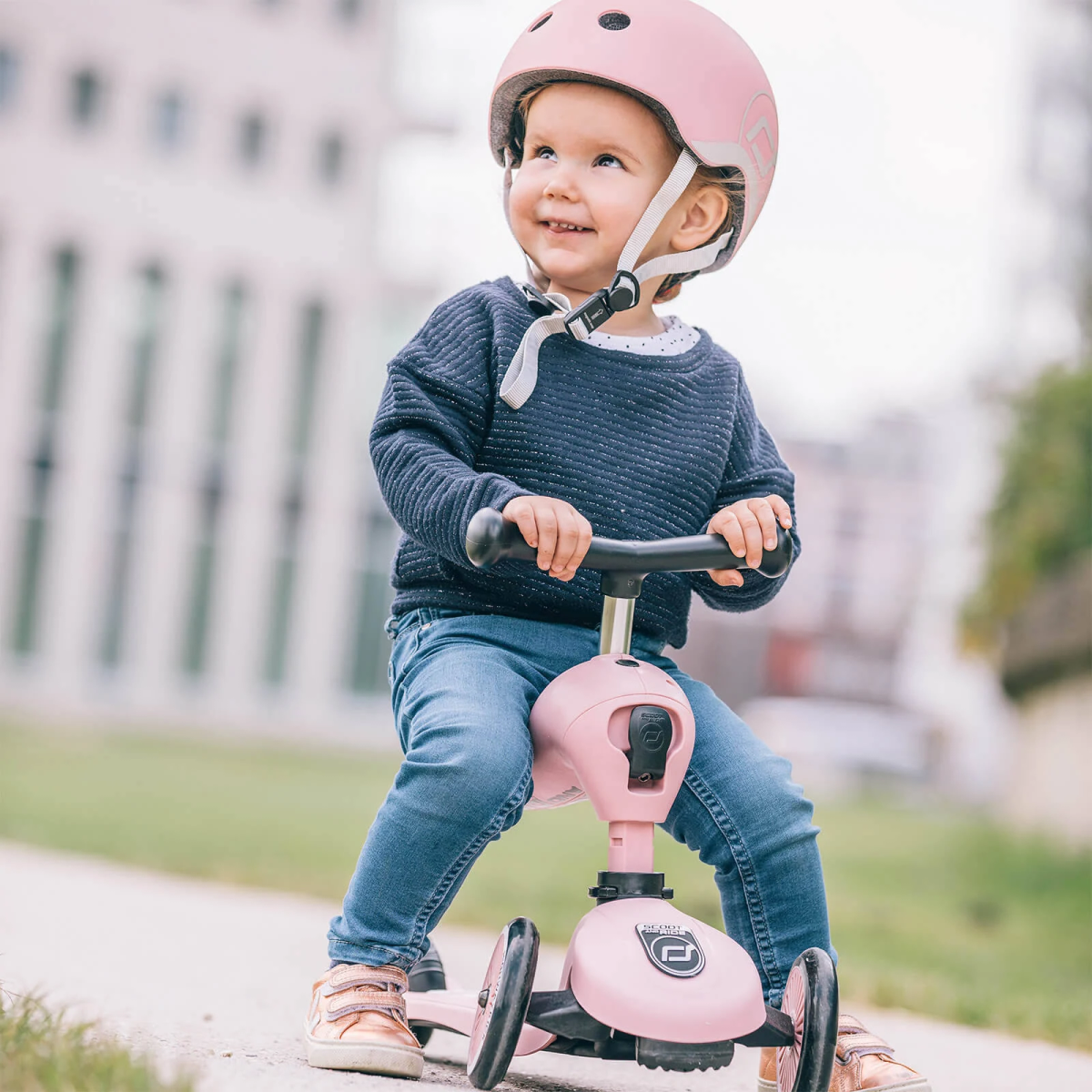 Un tout-petit portant un casque rose fait du trottinette rose.