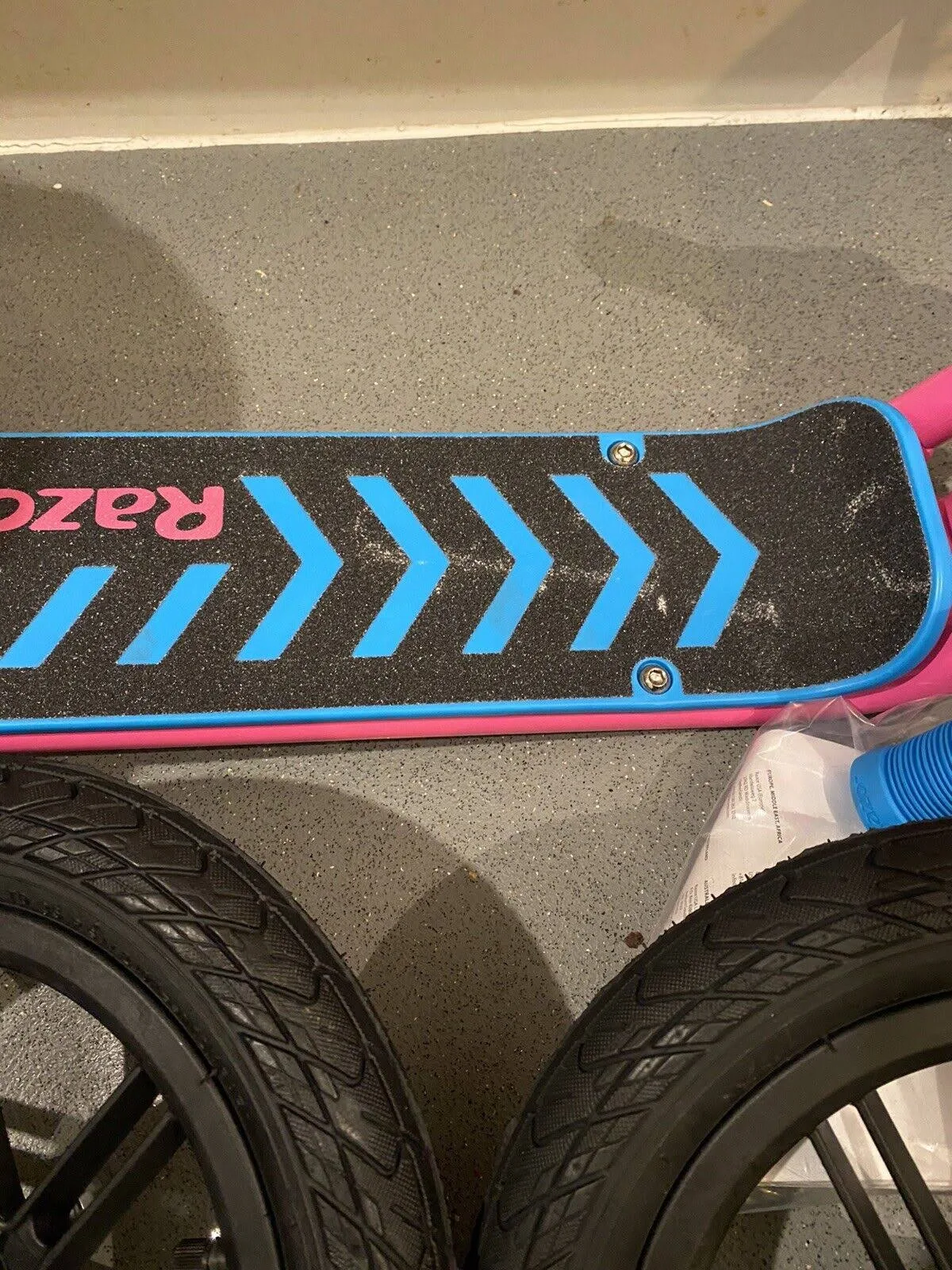 Platforma hulajnogi z niebieskimi wzorami w szewrony, różowymi obramowaniami i czarnymi kołami.