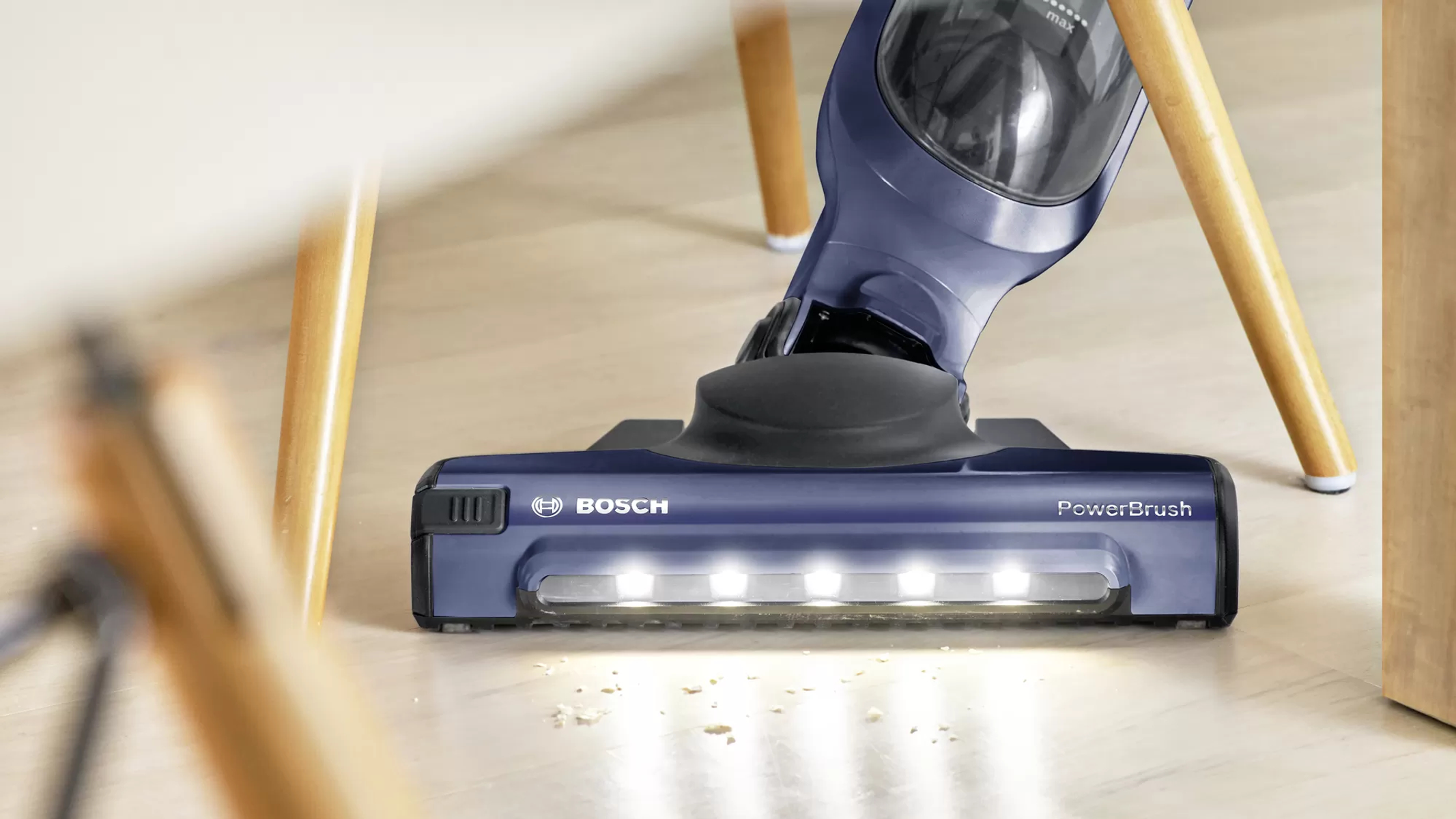 Testa di aspirapolvere blu su pavimento in legno, con polvere visibile e fasci di luce.