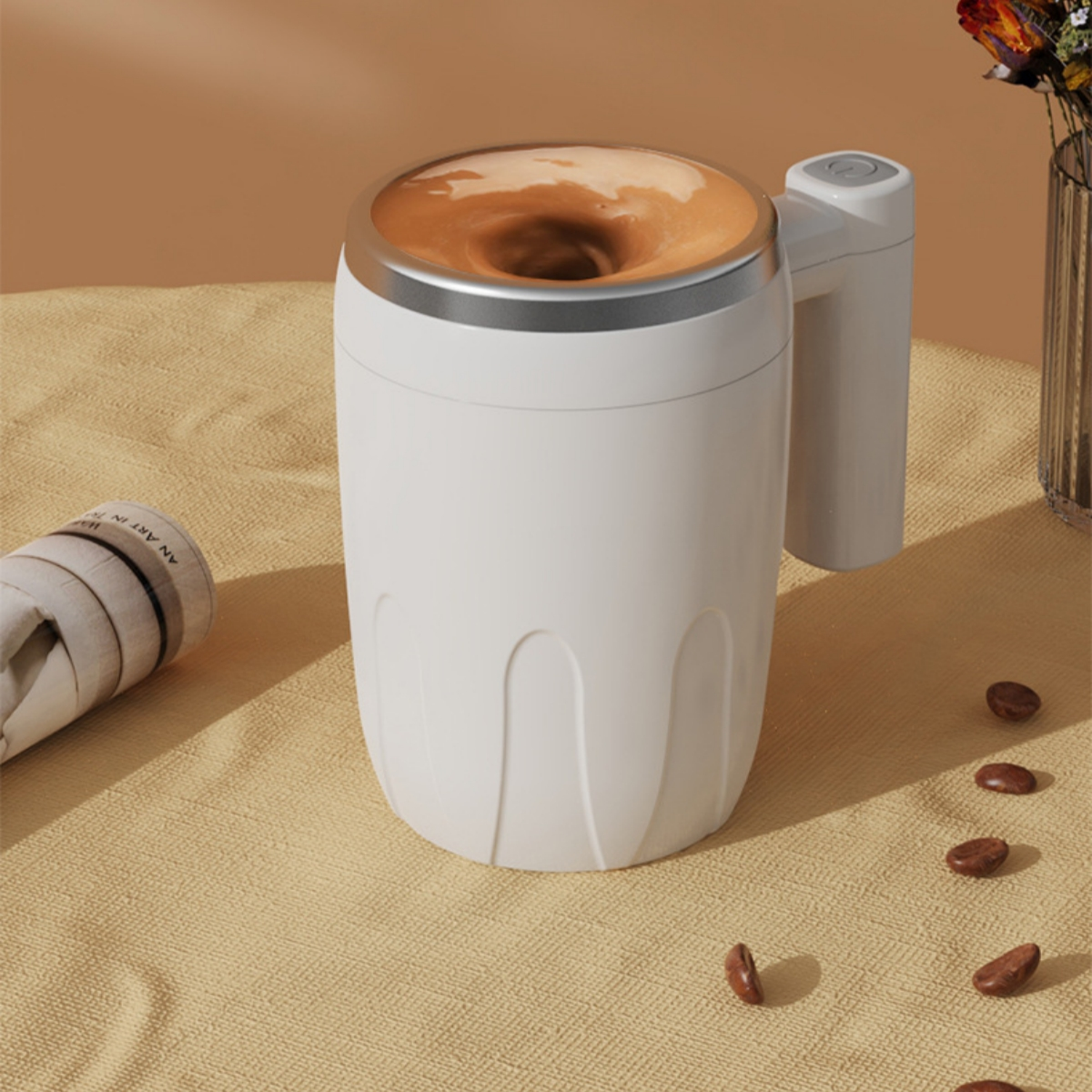 Weißer Becher mit gewirbeltem Kaffee, Griff sichtbar, Kaffeebohnen in der Nähe. Beige Oberfläche.