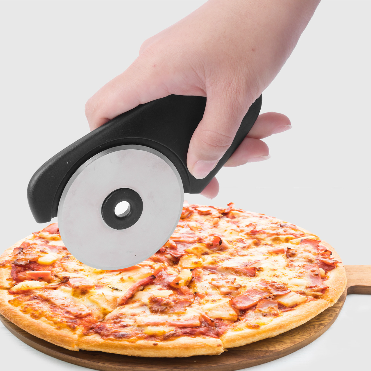 Eine Hand schneidet Pizza mit einem runden Pizzaschneider auf einem Holzbrett. Pizza ist in Scheiben geschnitten.
