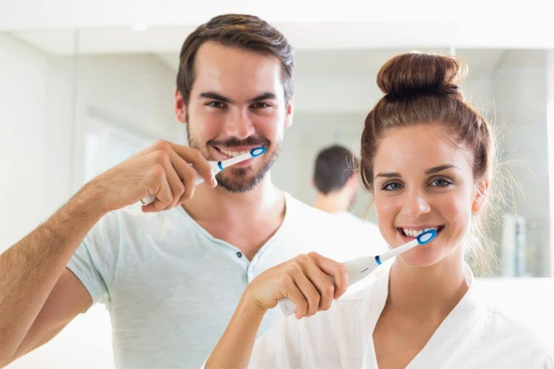 Una coppia si lava i denti insieme. Entrambi sorridono e usano spazzolini elettrici.