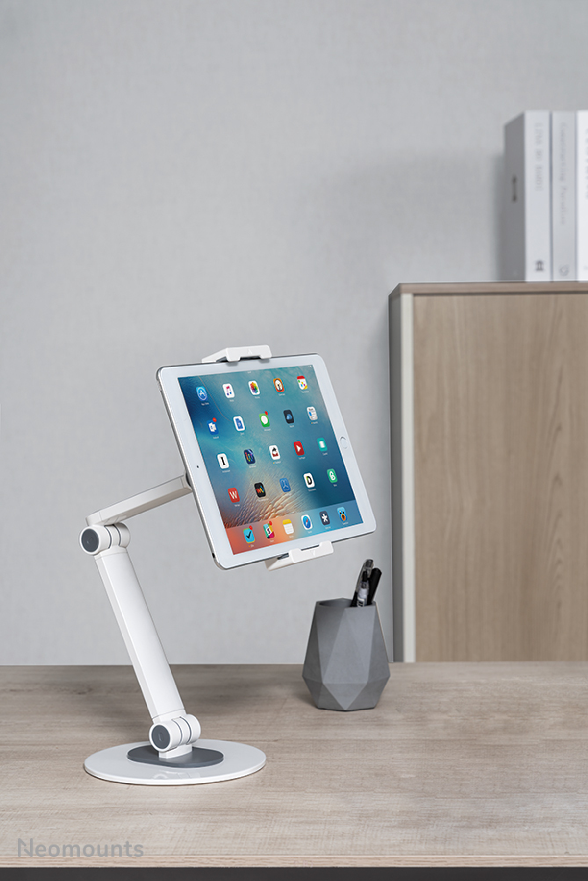 Tablet op een witte standaard. Het staat op een houten bureau. Grijze achtergrond.