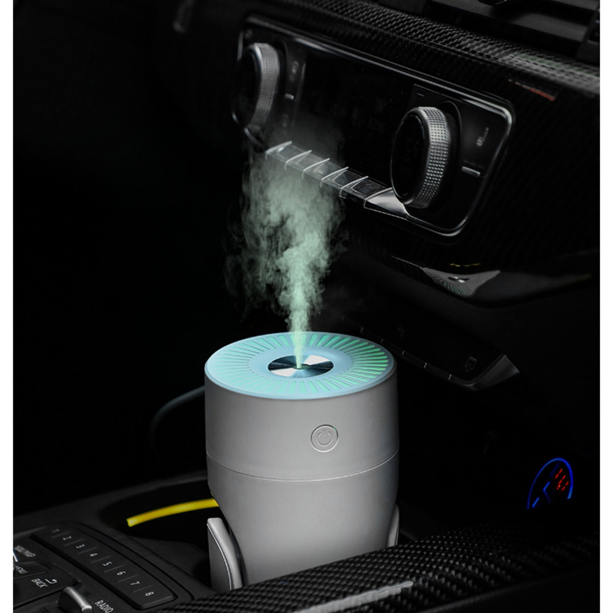 Ein kleiner, silberner Auto-Lufterfrischer, der Nebel abgibt, im Innenraum eines Autos.