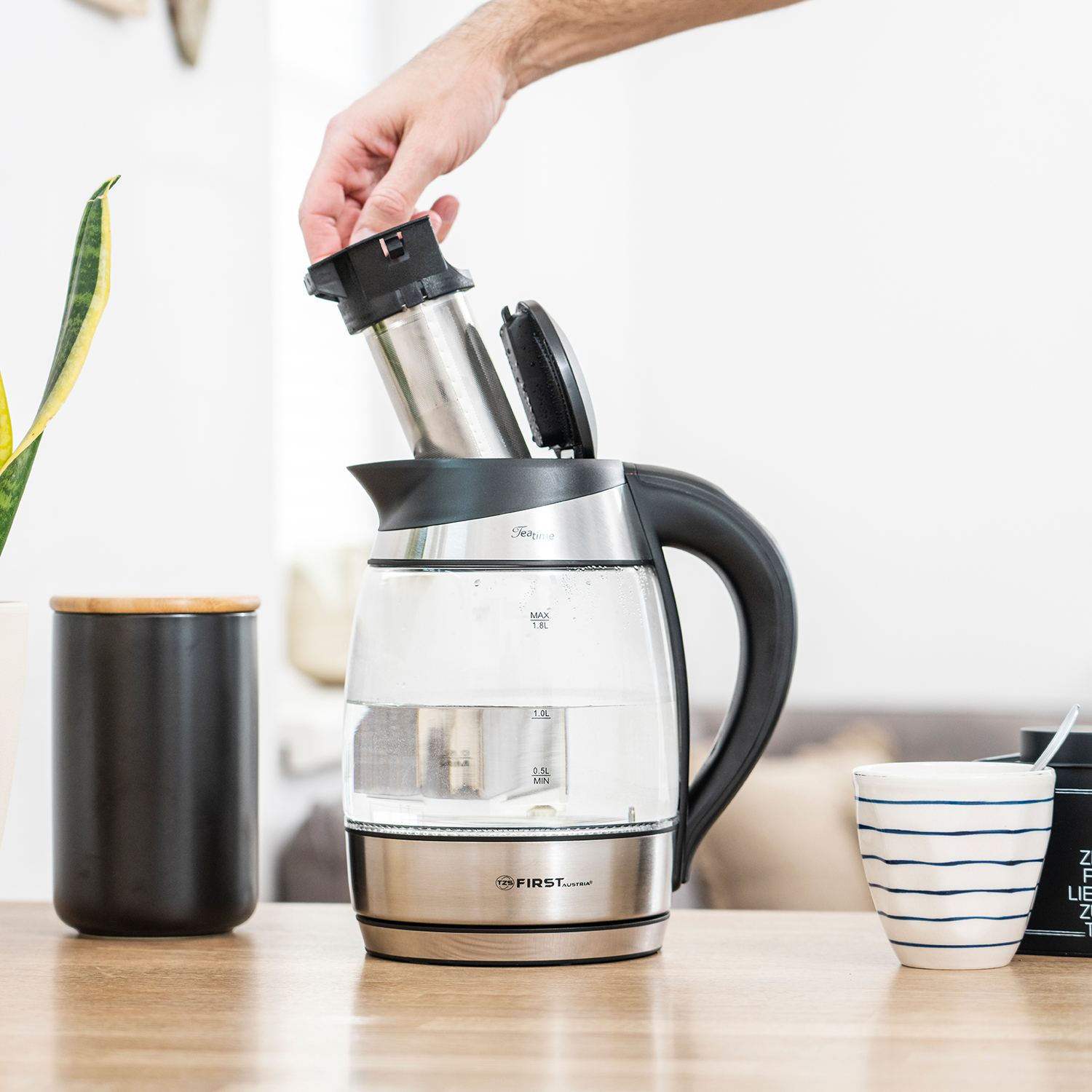 Eine Person fügt einen Tee-Infuser zu einem gläsernen Teekessel hinzu.