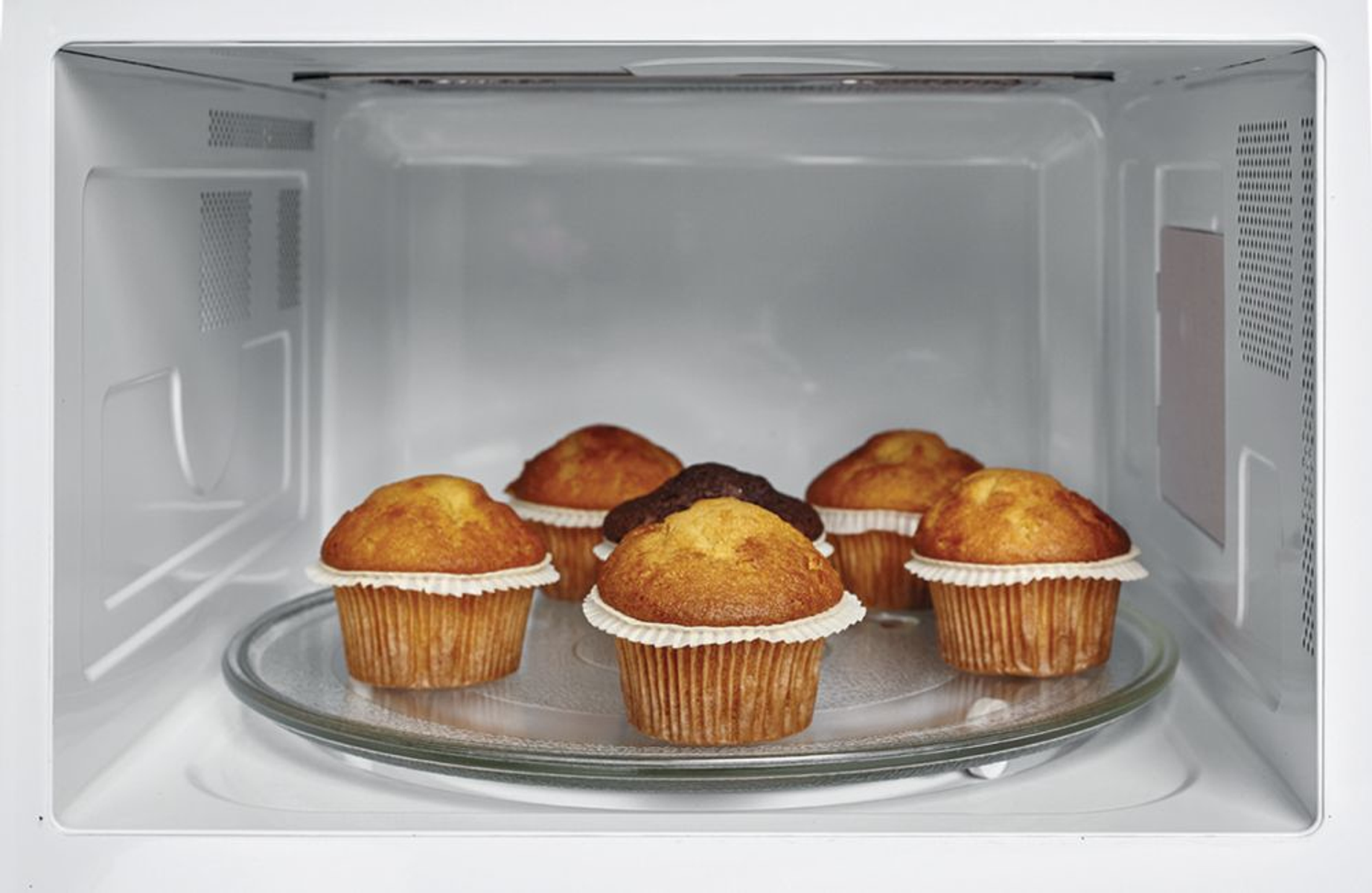 Sei muffin in un microonde su un piatto di vetro. I muffin sono in pirottini di carta.
