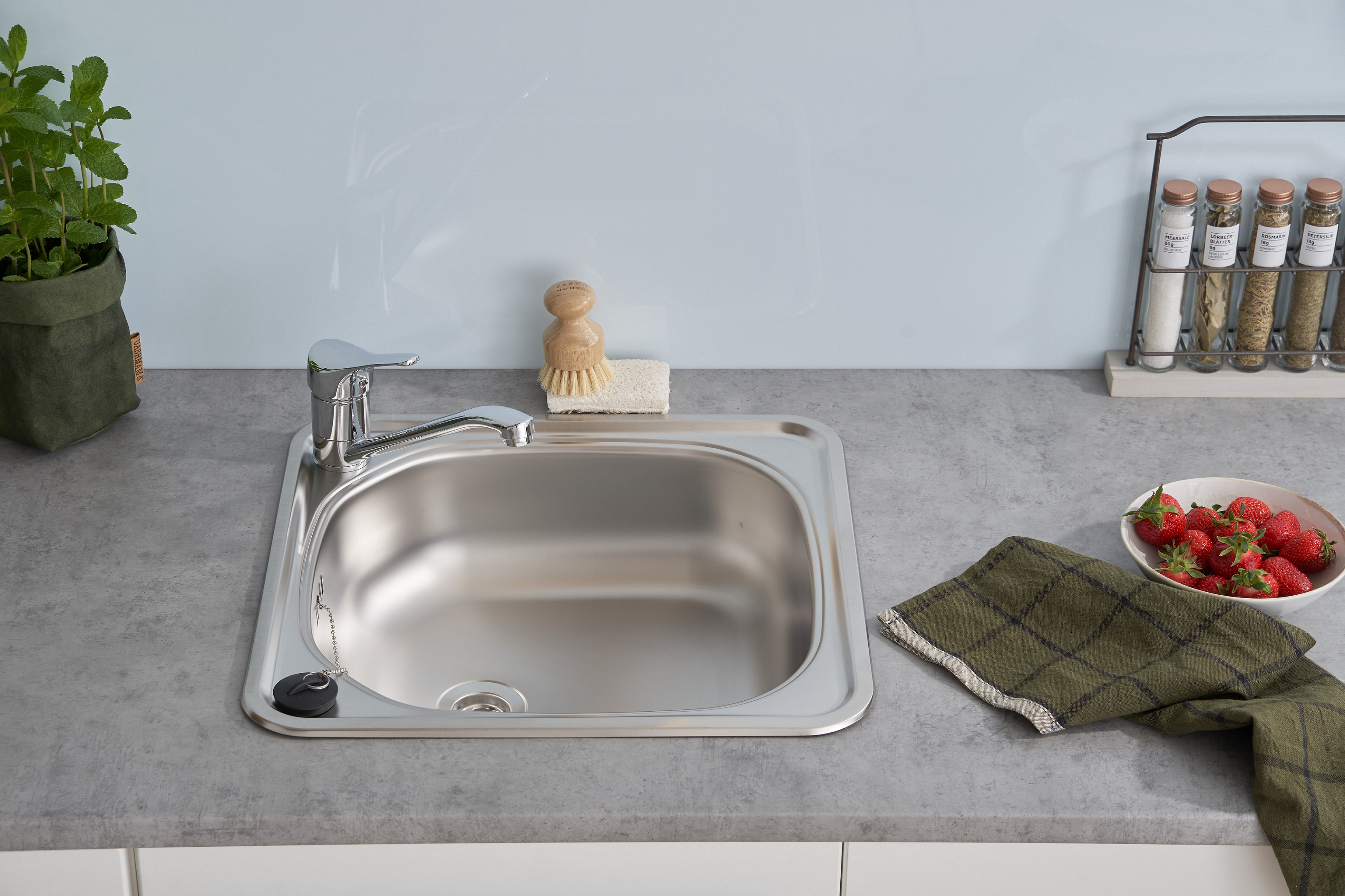 Ein Küchenspülbecken mit Wasserhahn, Spülbürste, Schwamm und Erdbeeren auf einer Arbeitsplatte.