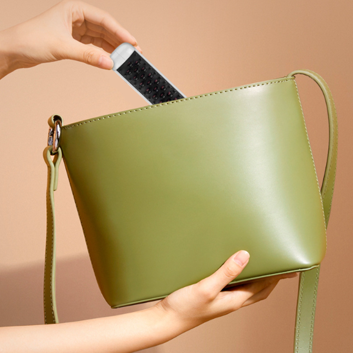 Eine Hand legt eine schwarze Fernbedienung in eine grüne Ledertasche. Beiger Hintergrund.