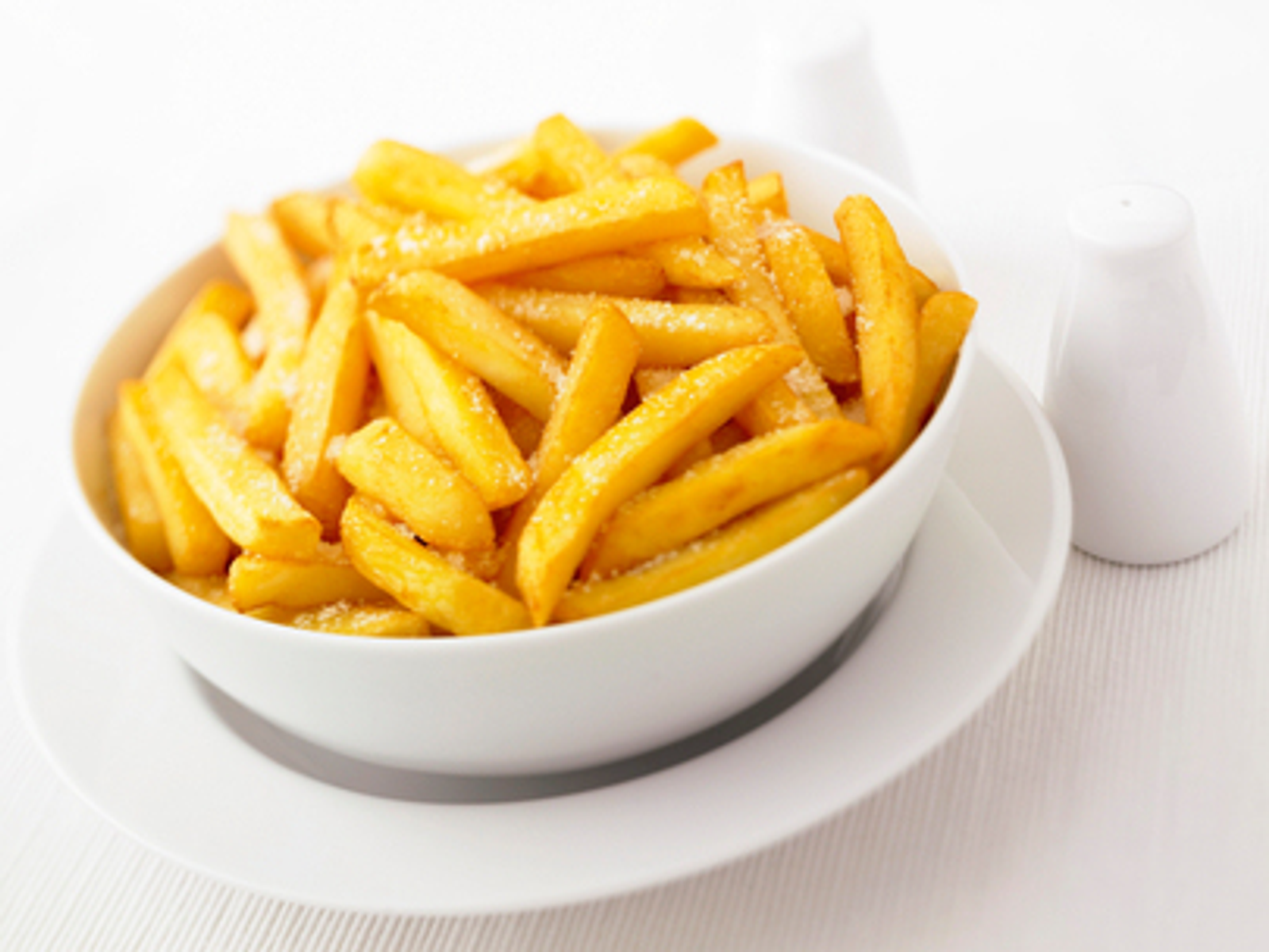 Miska złotych frytek. Frytki posypane są solą, na białym talerzu.