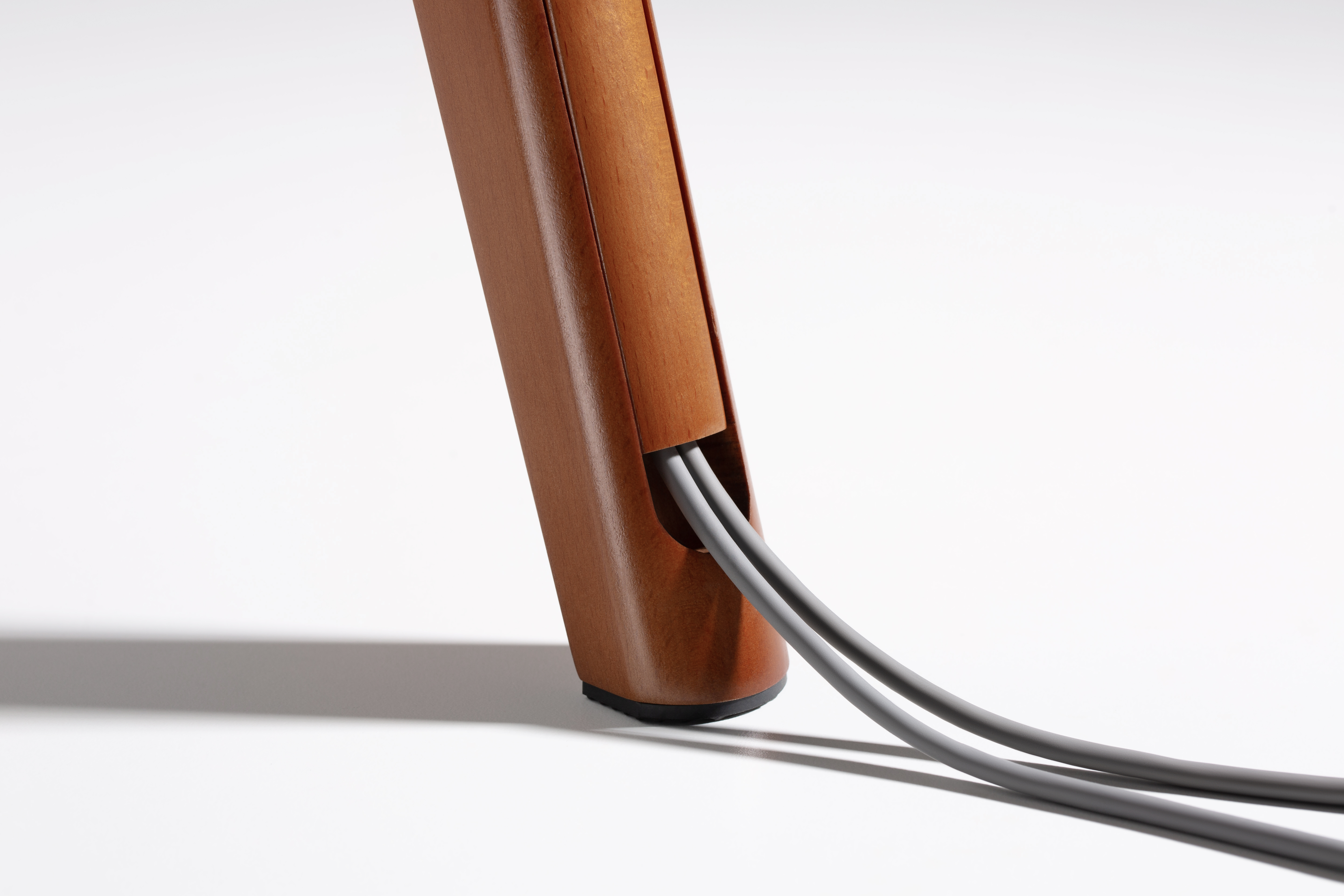 Primer plano de una pata de mesa de madera. Dos cables grises salen de la parte inferior de la pata.