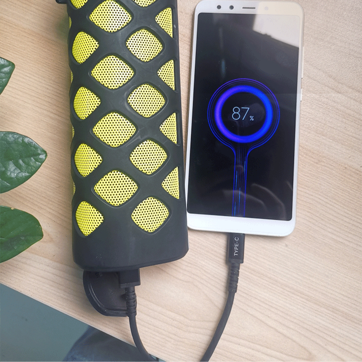 Ein Lautsprecher und ein weißes Smartphone, das über ein USB-C-Kabel geladen wird. Das Telefon zeigt 87% Akku.