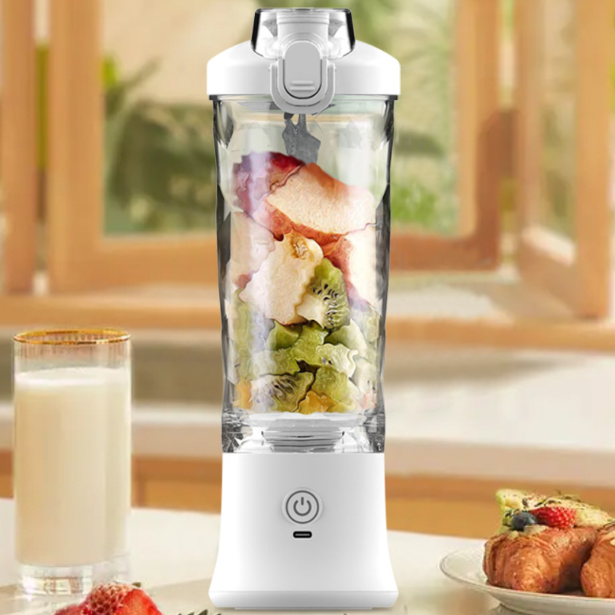 Ein weißer Mixer mit Früchten darin, sowie ein Glas Milch und ein Gebäck daneben.
