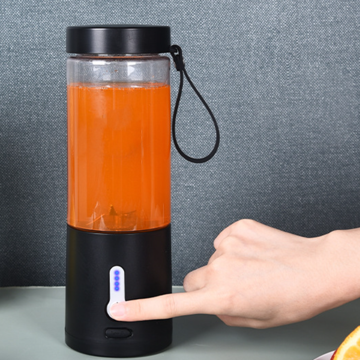 Eine Hand drückt einen Knopf an einem schwarzen und durchsichtigen Mixer mit orangener Flüssigkeit.