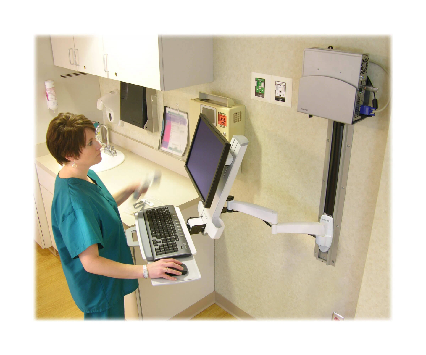 Infirmière à un bureau avec un moniteur, un clavier et une configuration de bras d'ordinateur.