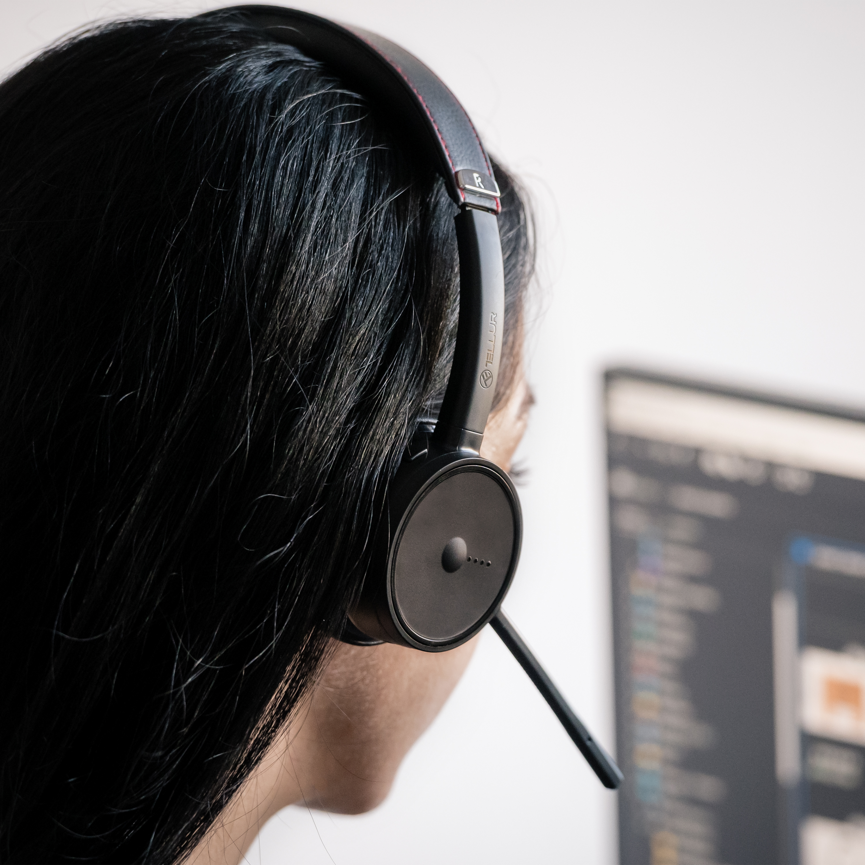 Frau mit schwarzem Headset. Fokus auf ihrem Hinterkopf und dem Headset. Weißer Hintergrund.