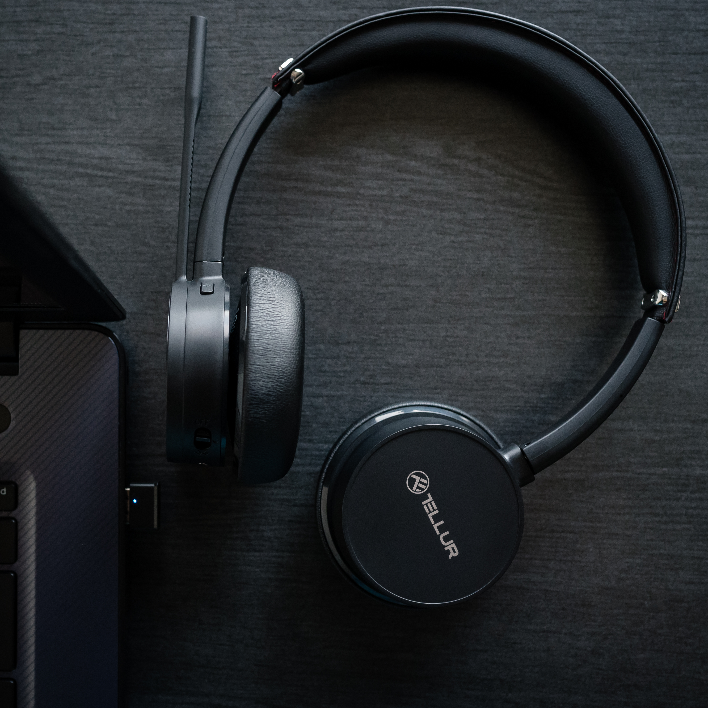 Schwarzes Tellur-Headset und ein USB-Dongle auf dunkler Holzoberfläche, Draufsicht.