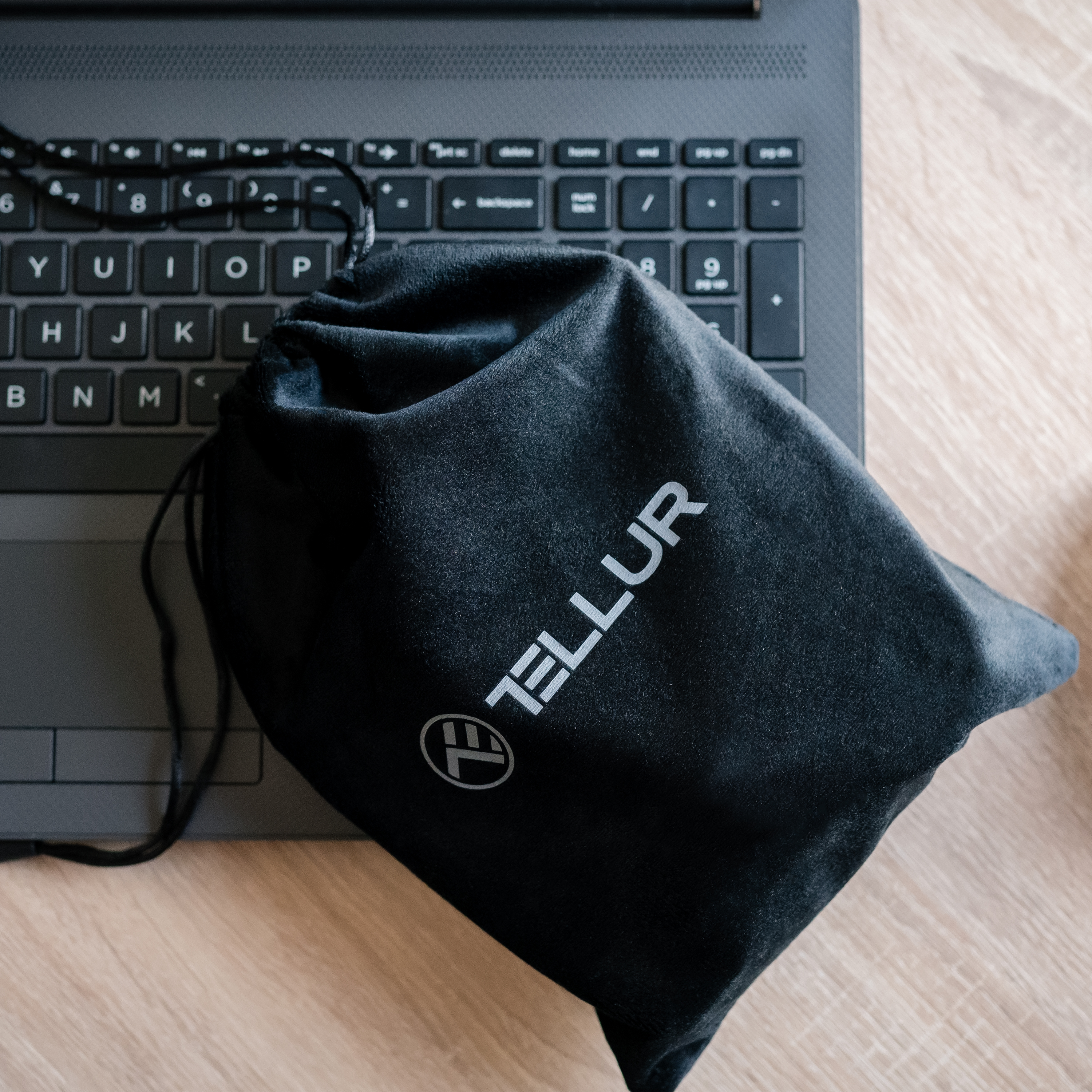 Eine schwarze Tasche mit der Aufschrift 'TELLUR' neben einem Laptop. Die Tasche liegt auf Holz.
