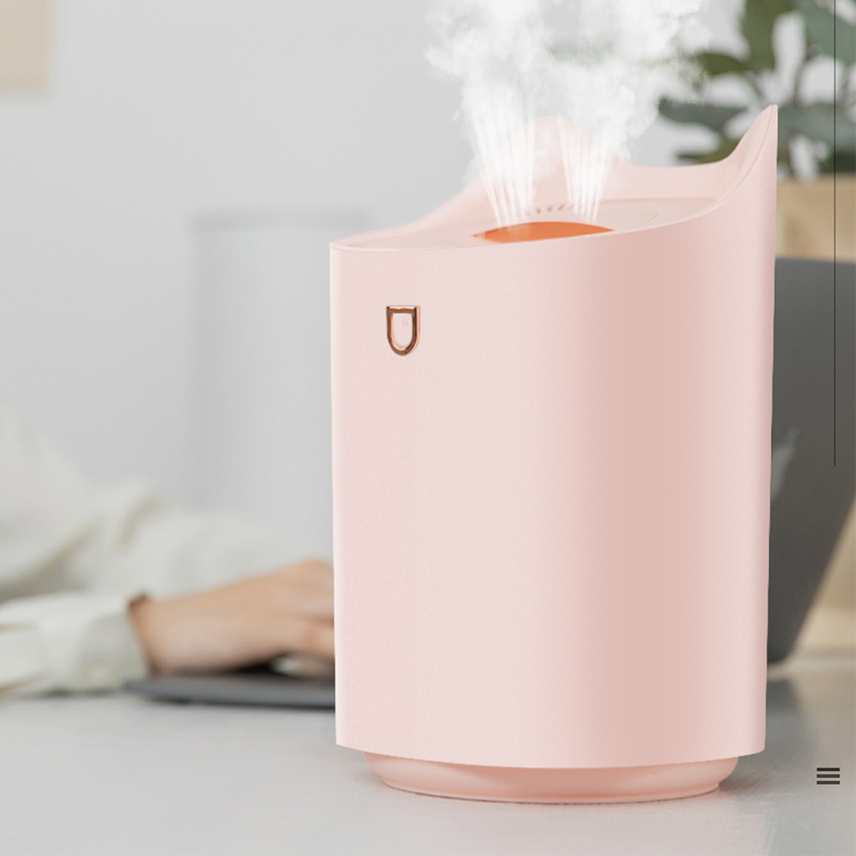 Rosa Luftbefeuchter mit Dampf, neben einem Schreibtisch mit Laptop.