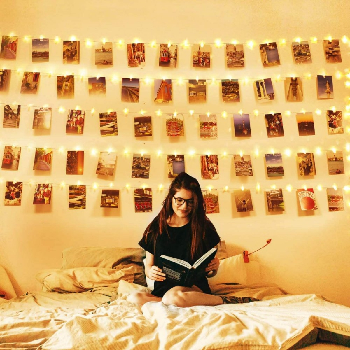 Frau im Bett liest mit Lichterketten. Wand mit Fotos.