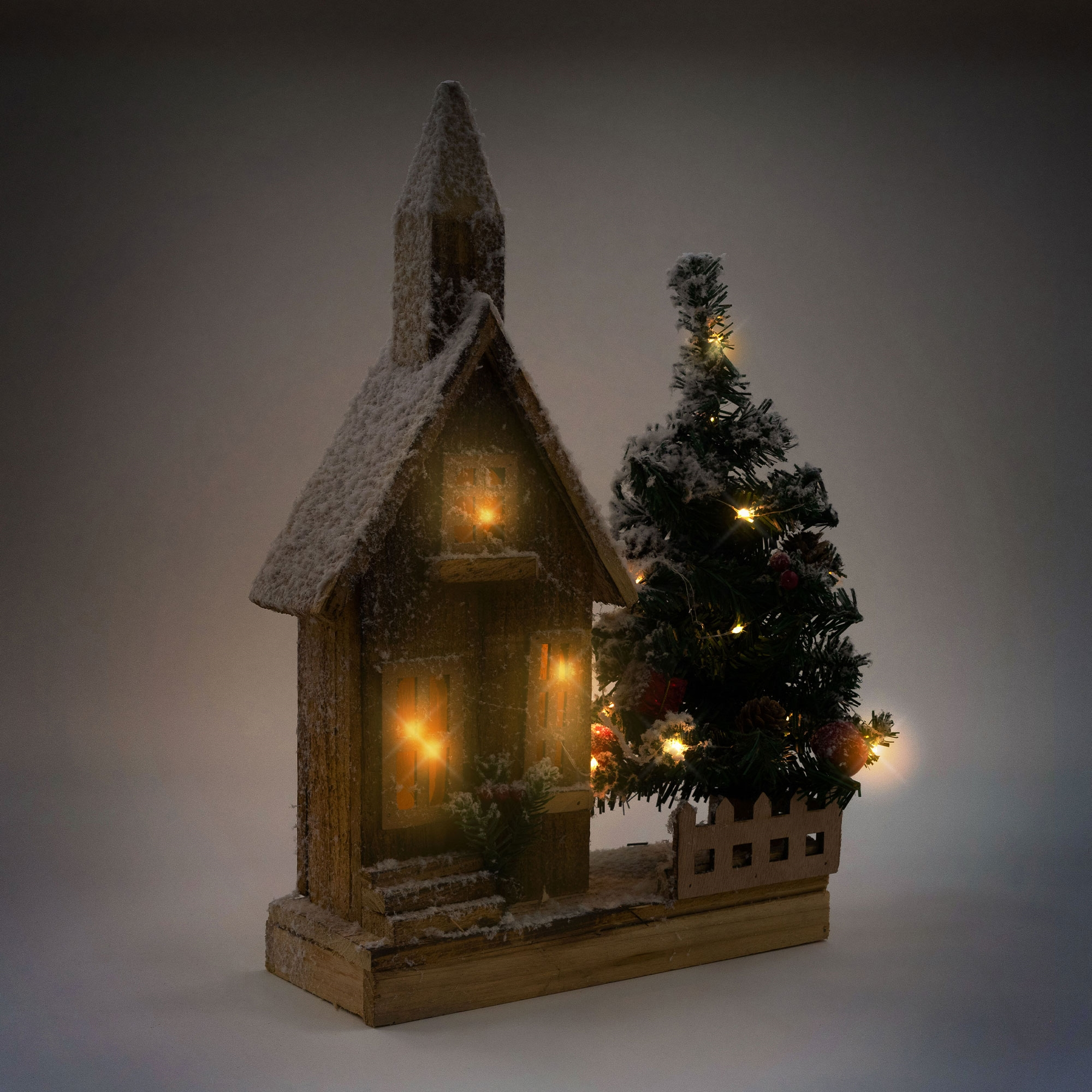 Weihnachtliche Kirchendekoration mit Lichtern. Die Kirche hat einen kleinen Baum und Schnee. Es ist innen beleuchtet.