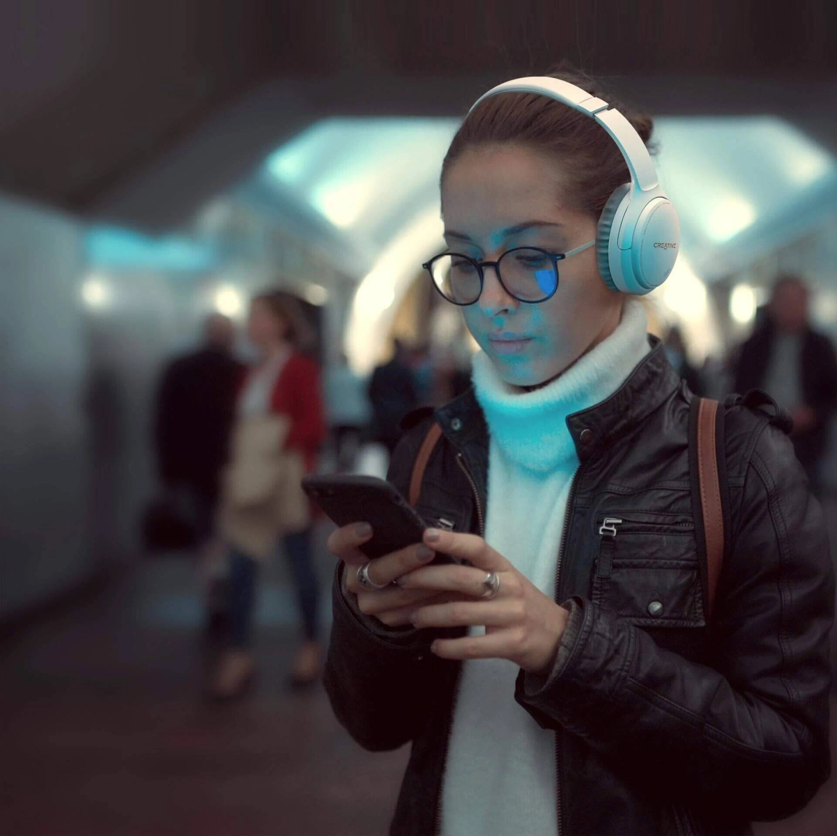 Frau mit Brille und Kopfhörern, die ein Telefon in einer U-Bahn benutzt. Verschwommener Hintergrund.