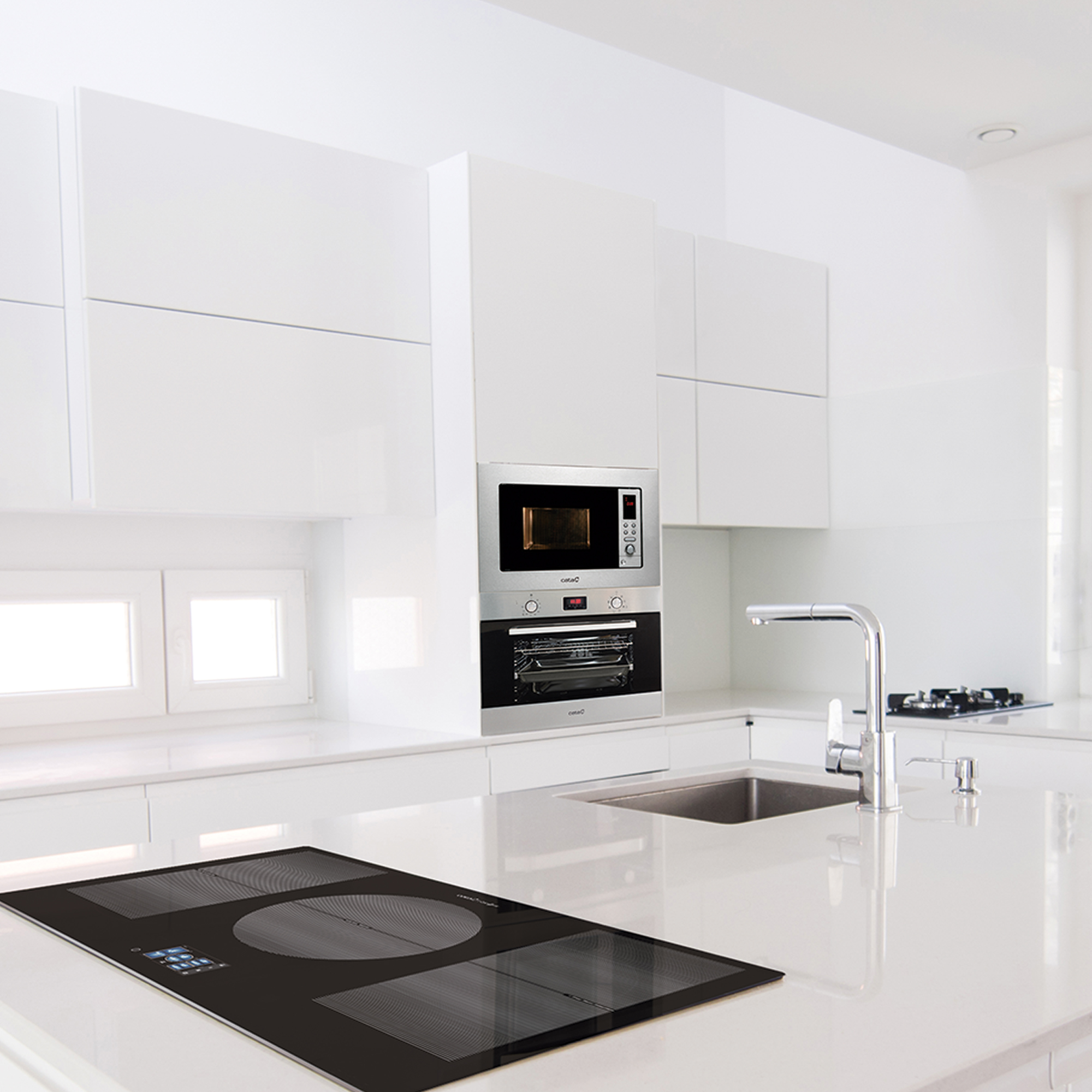 Cucina bianca moderna con isola. Forno e microonde incassati. Piano cottura nero sull'isola.